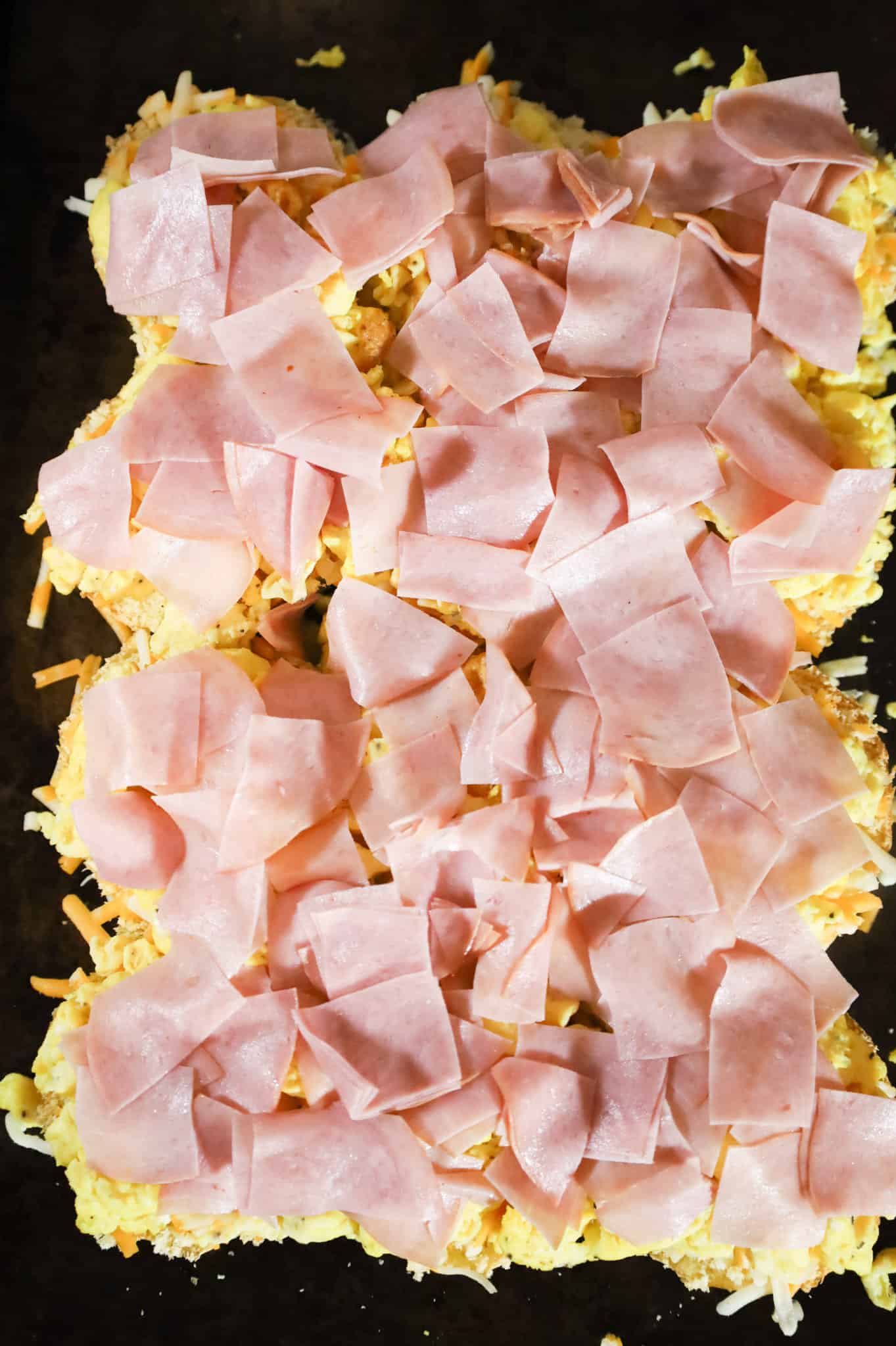 chopped ham on top of scrambled eggs and shredded cheese on a baking sheet