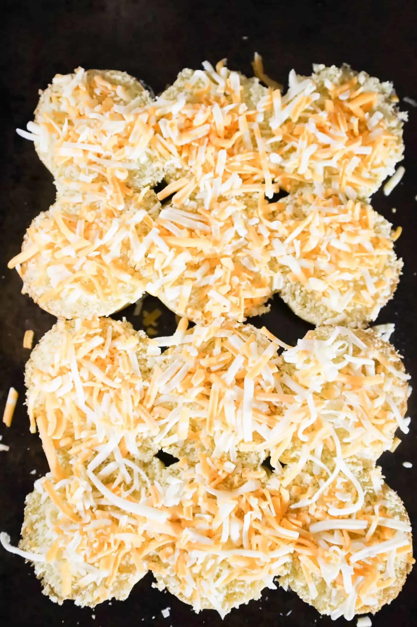 shredded cheese on slider buns on a baking sheet