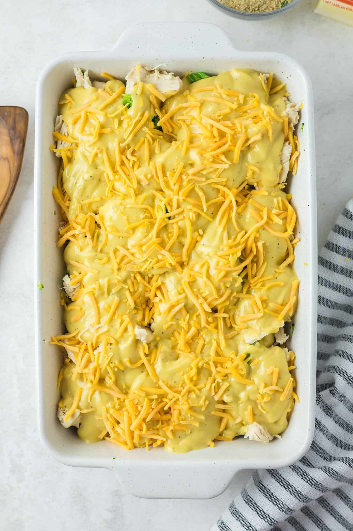 shredded cheddar cheese sprinkled on top of soup, chicken and broccoli in a baking dish