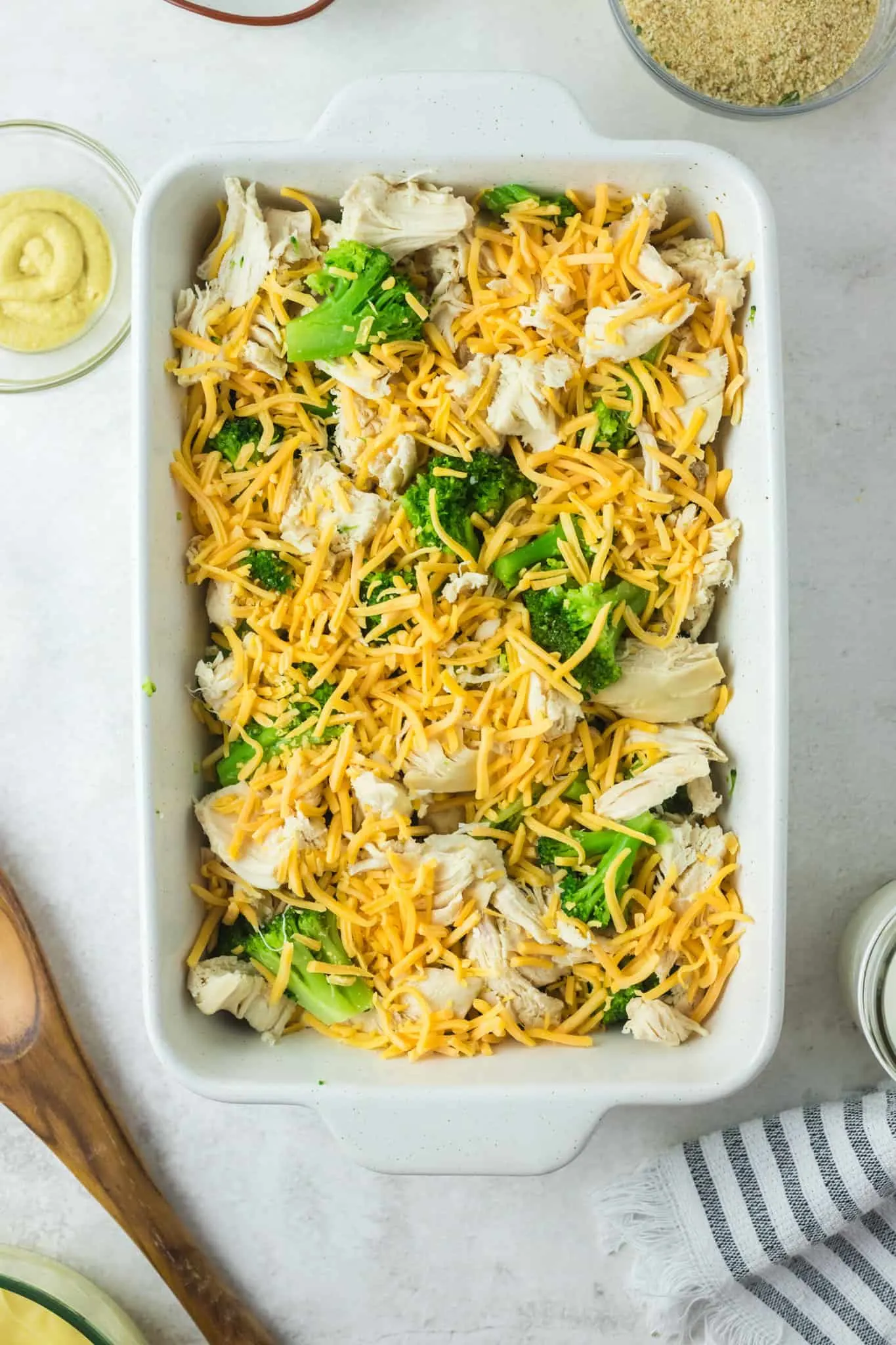 shredded cheddar cheese on top of chopped chicken and broccoli florets in a baking dish