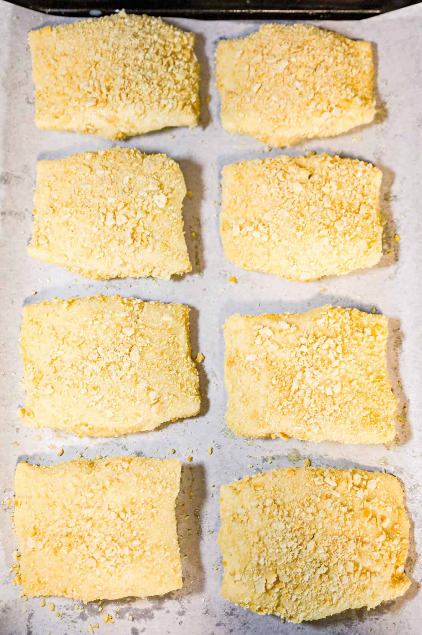 Ritz cracker crumb coated chicken pillows on a parchment lined baking sheet
