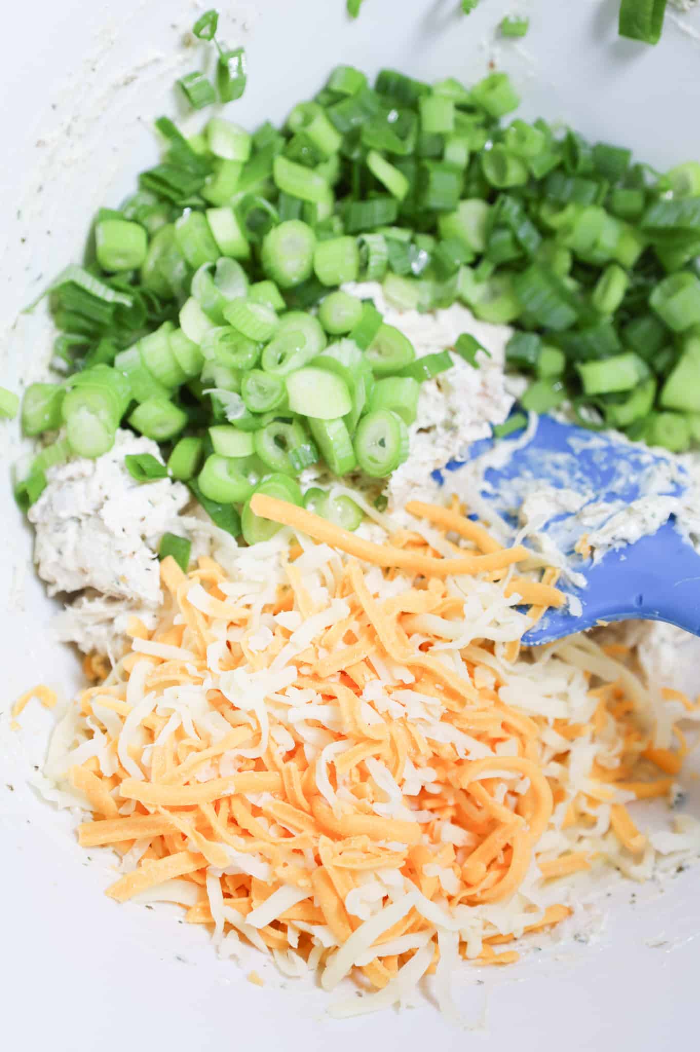 chopped green onions and shredded cheese on top of creamy chicken mixture in a mixing bowl