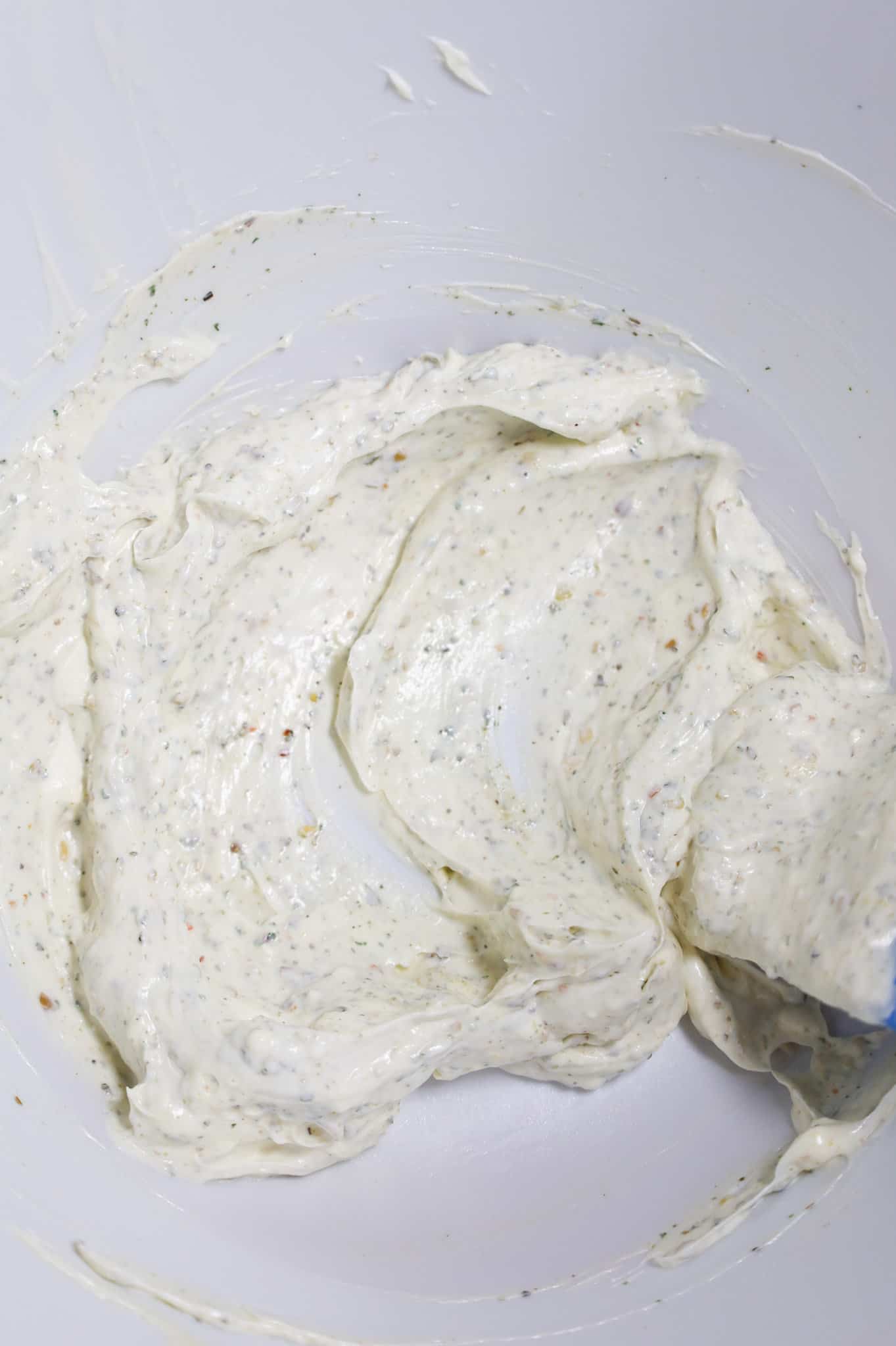 Italian seasoning stirred into sour cream and mayo mixture in a mixing bowl