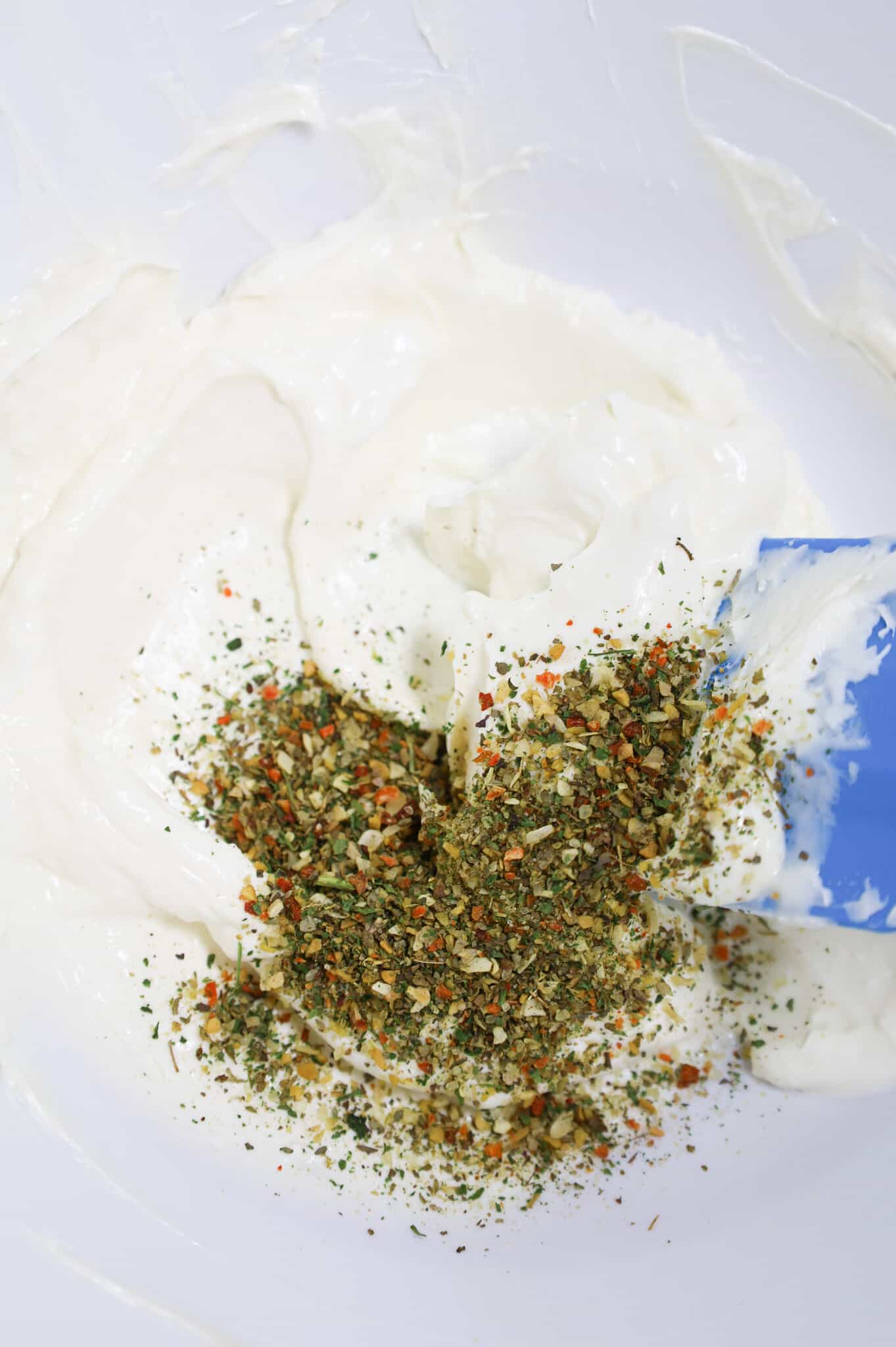 Italian seasoning added to bowl with sour cream and mayo mixture
