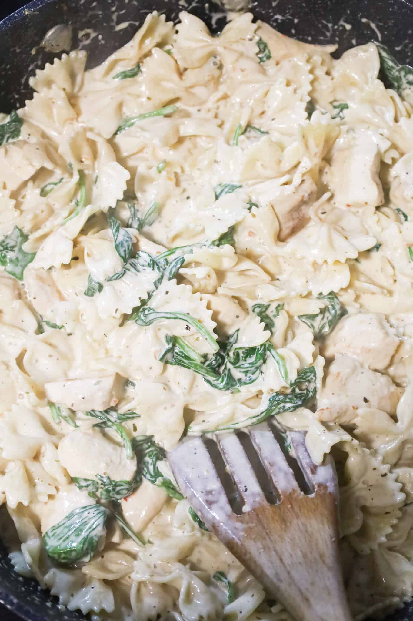 spinach alfredo pasta being stirred in a skillet