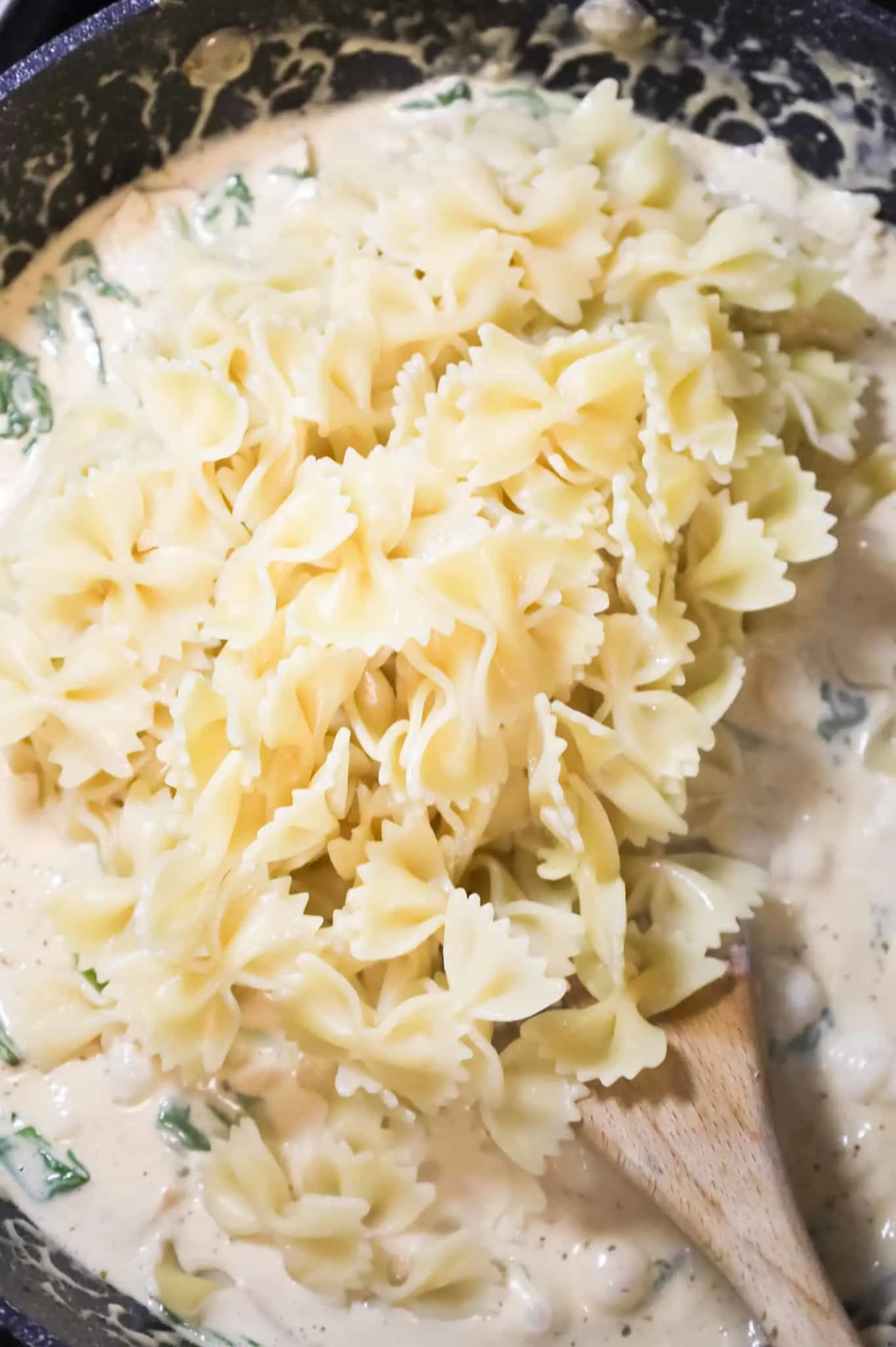 cooked bowtie noodles added to skillet with alfredo sauce