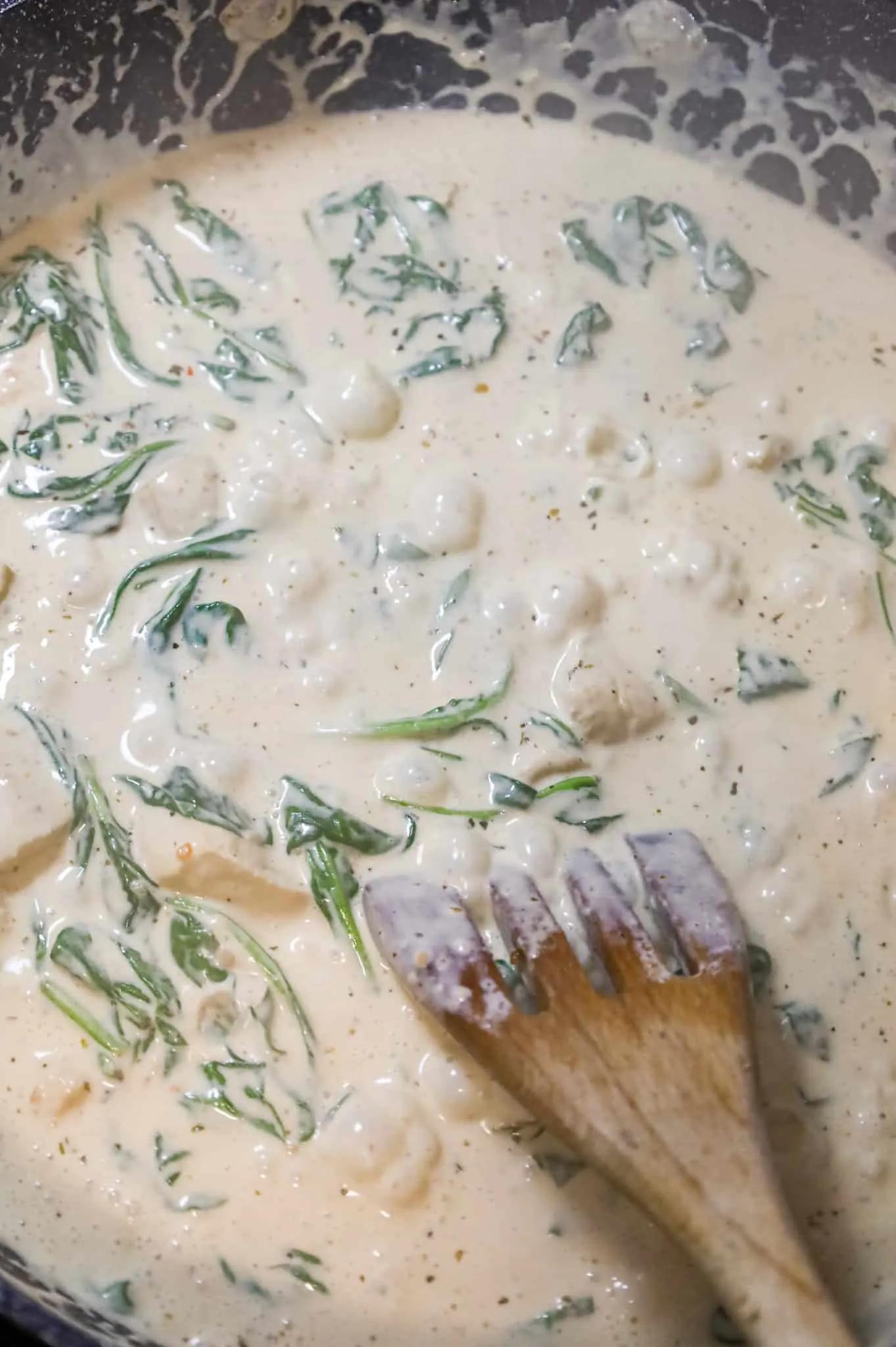 spinach wilting in alfredo sauce in a skillet