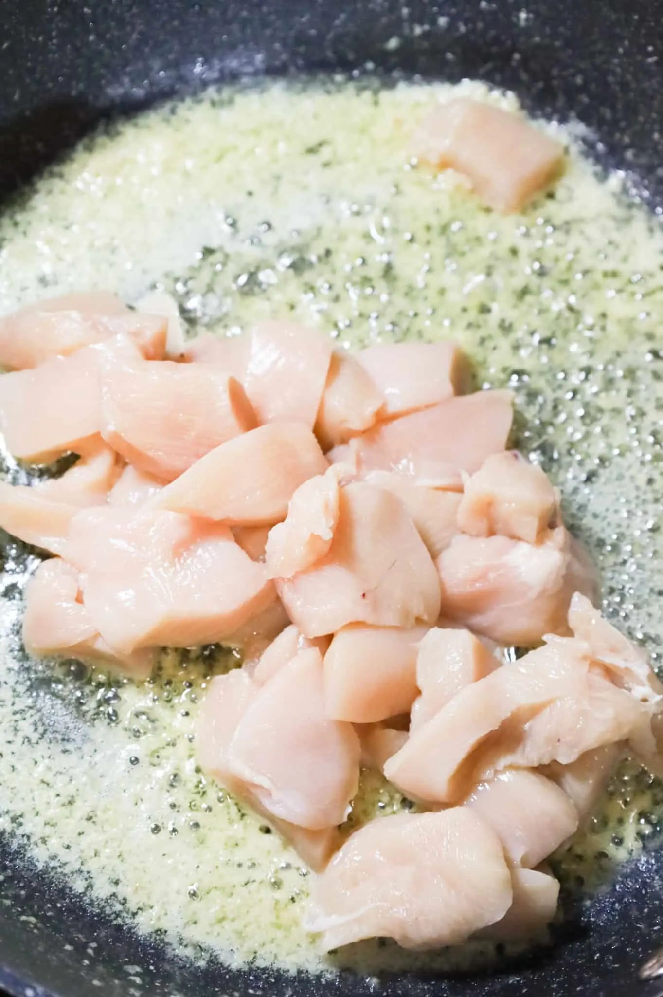raw chicken breast chunks in a skillet with melted butter and garlic in a skillet