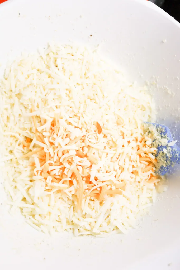 shredded cheese on top of shredded hashbrown potatoes in a large mixing bowl