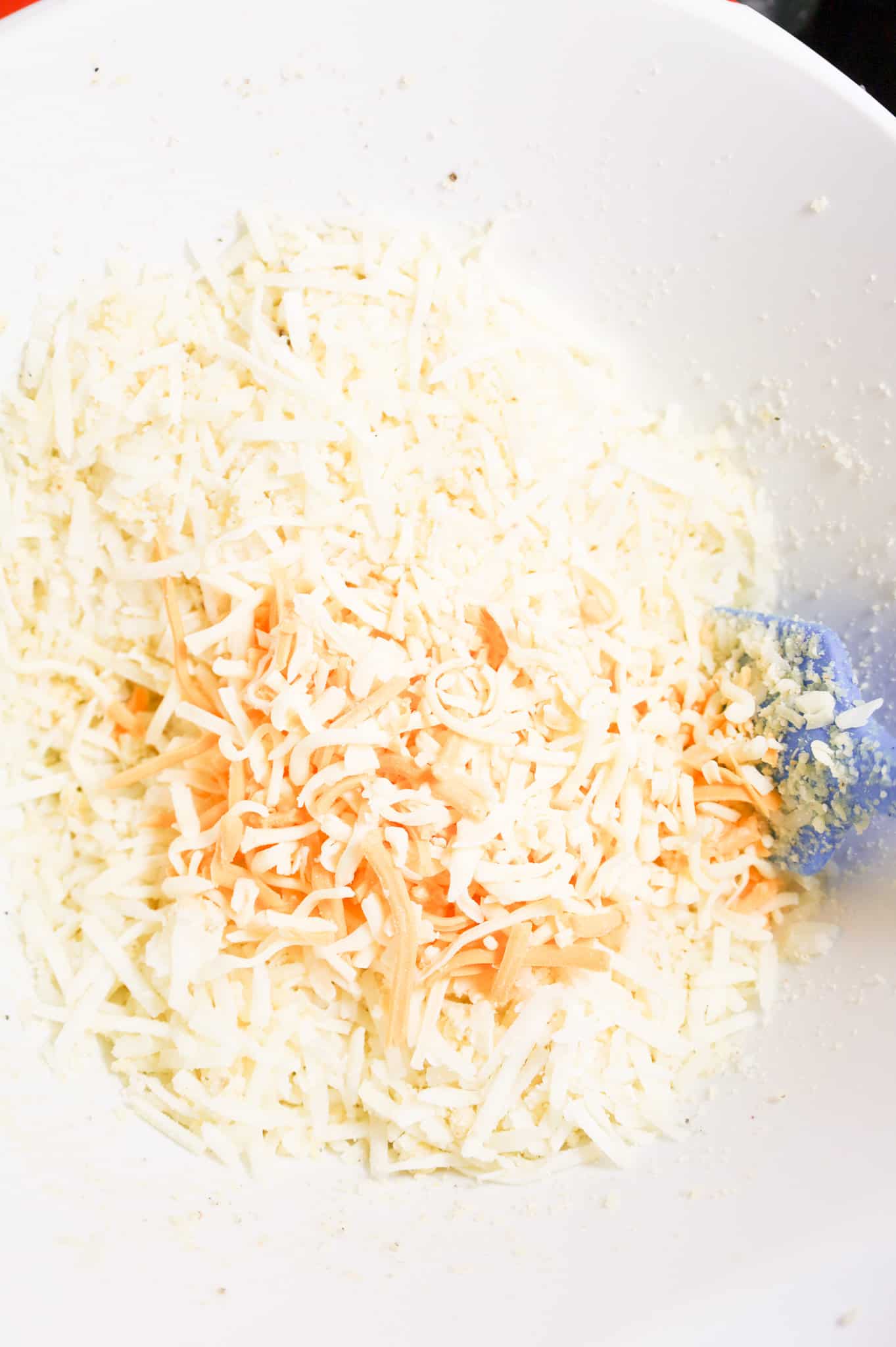 shredded cheese on top of shredded hashbrown potatoes in a large mixing bowl