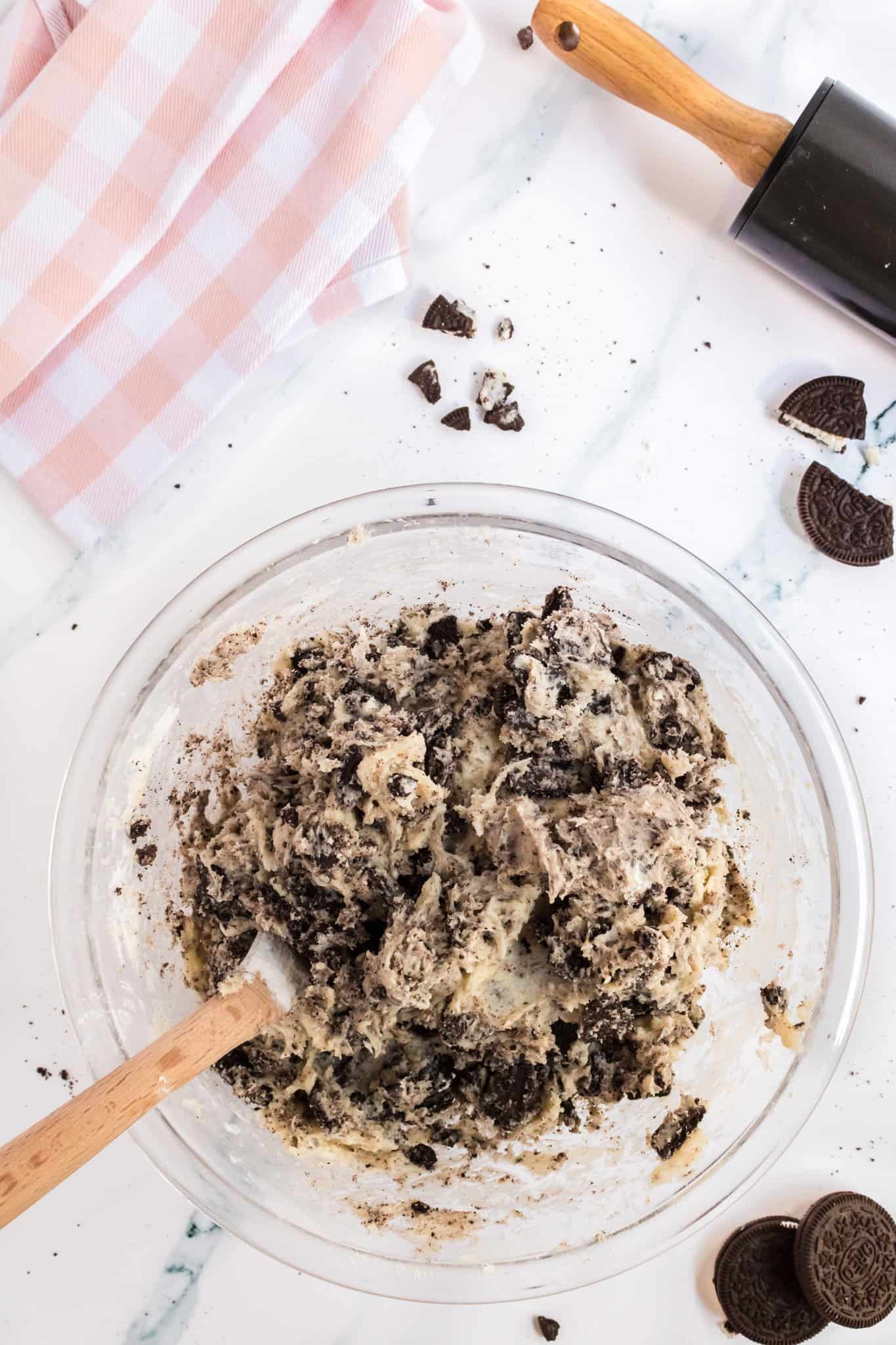 crumbled Oreos stirred into cookie dough in a mixing bowl
