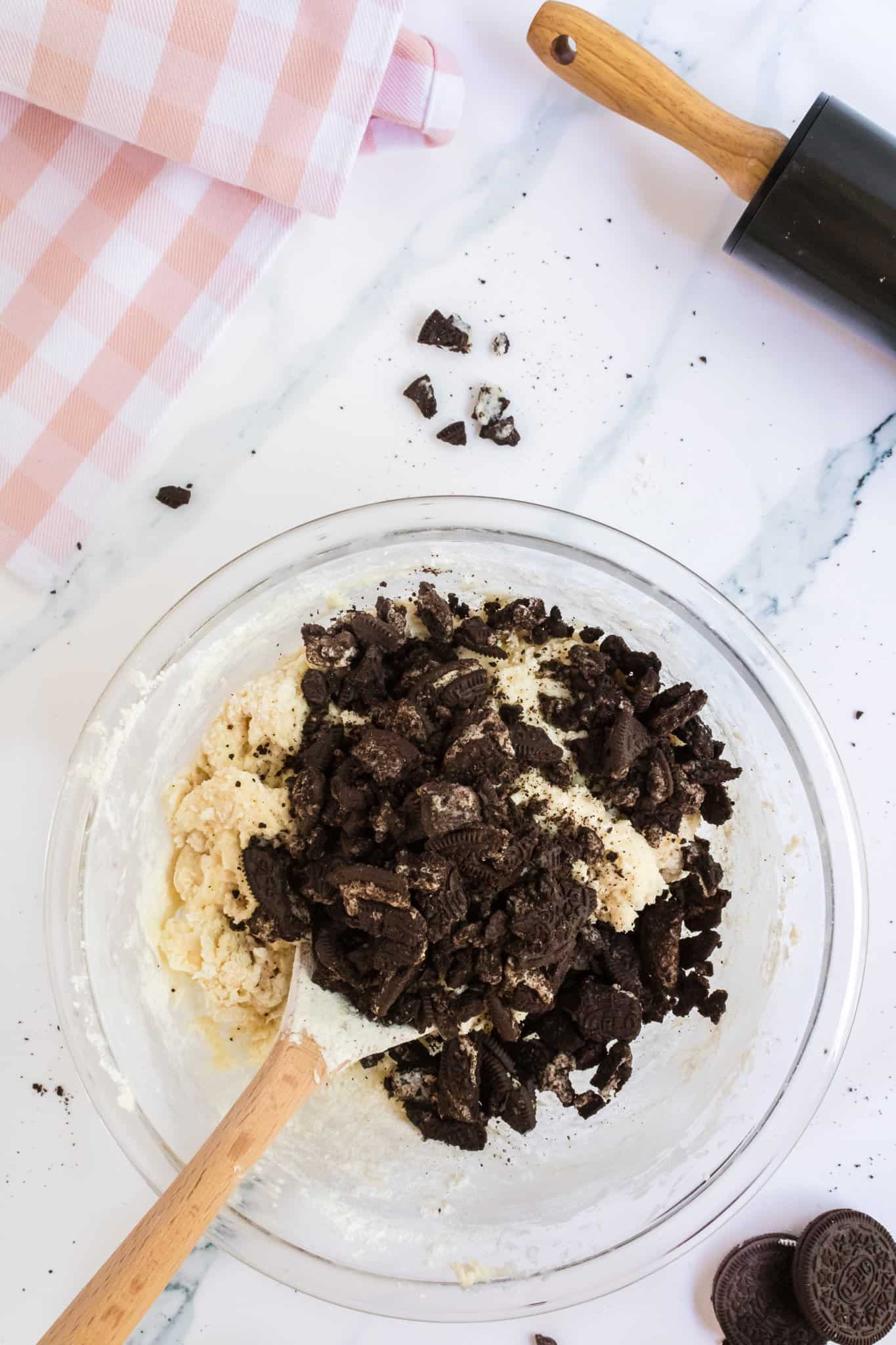 crushed Oreos added to cheesecake cookie dough in a mixing bowl