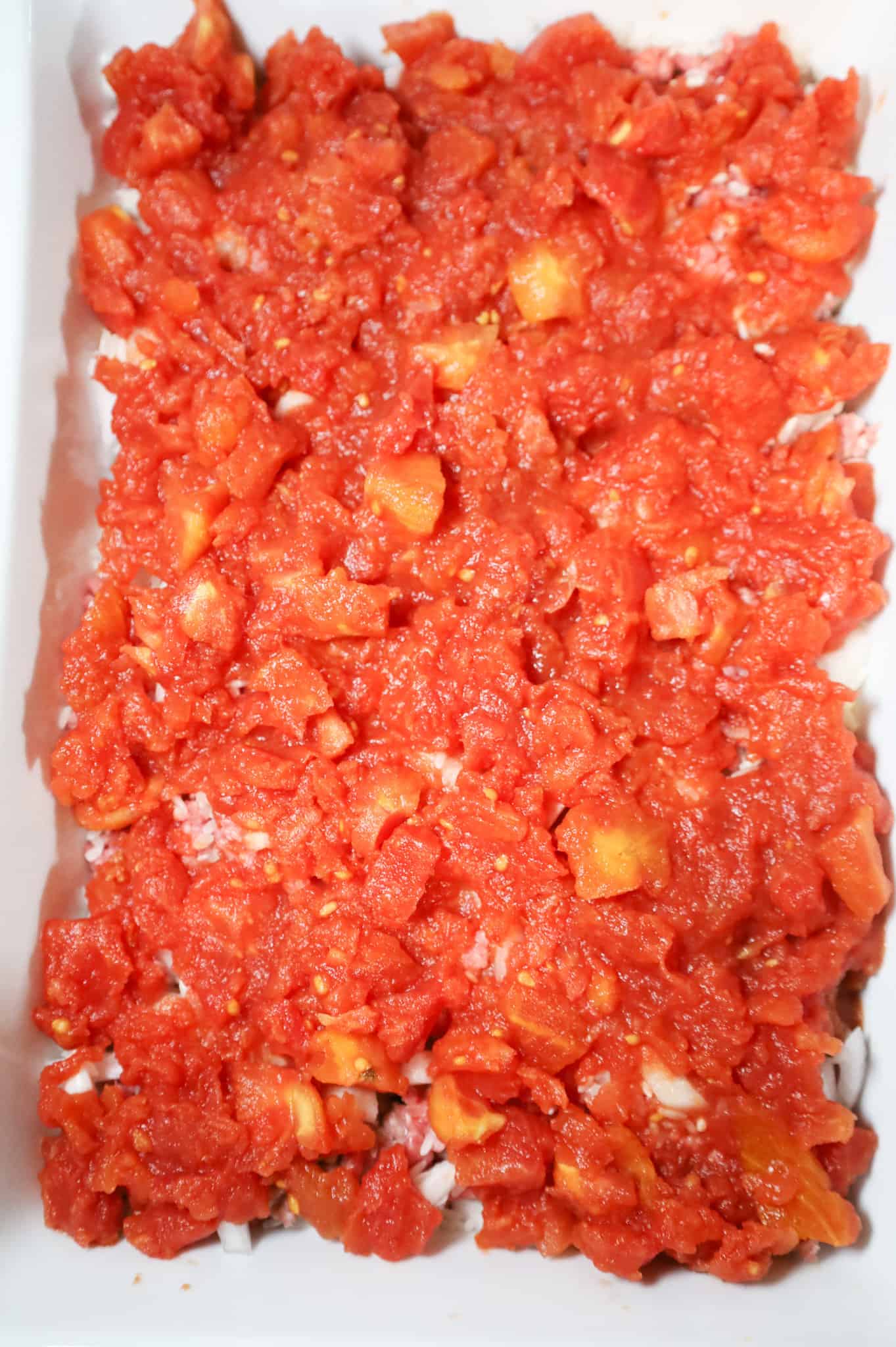 diced tomatoes on top of ground beef and potatoes in a casserole dish