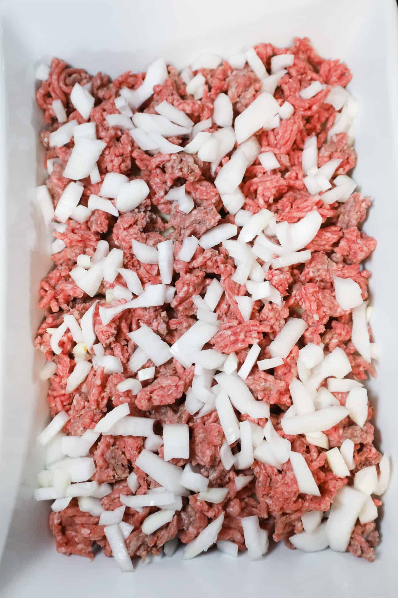 diced onions on top of raw ground beef in a casserole dish