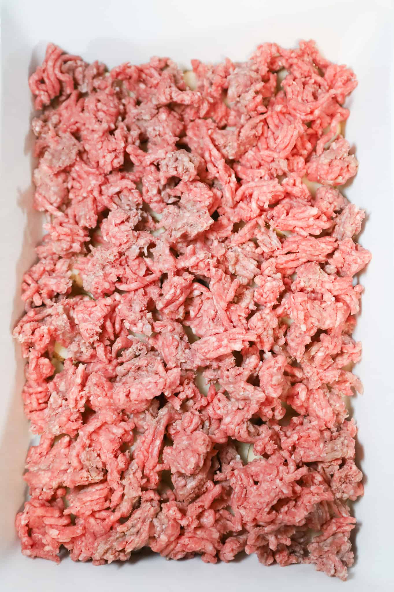 raw ground beef on top of sliced potatoes in a casserole dish