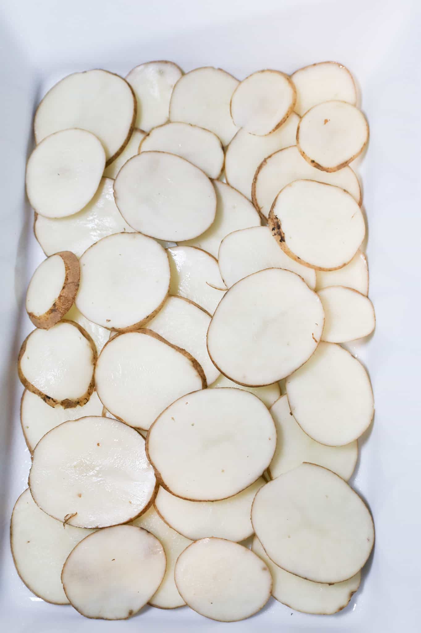 sliced potatoes in the bottom of a casserole dish