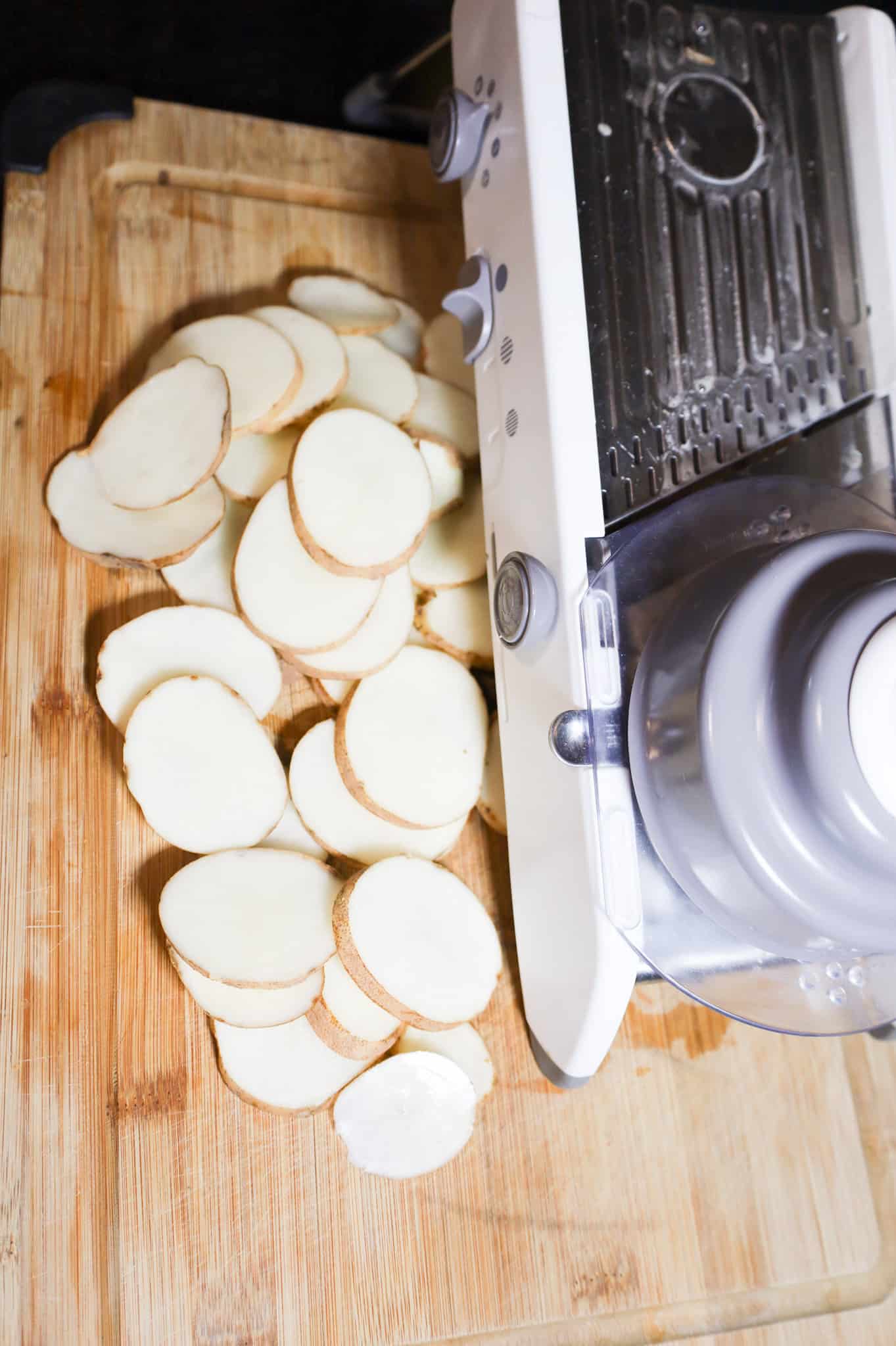 sliced potatoes and a mandoline slicer on a cutting board