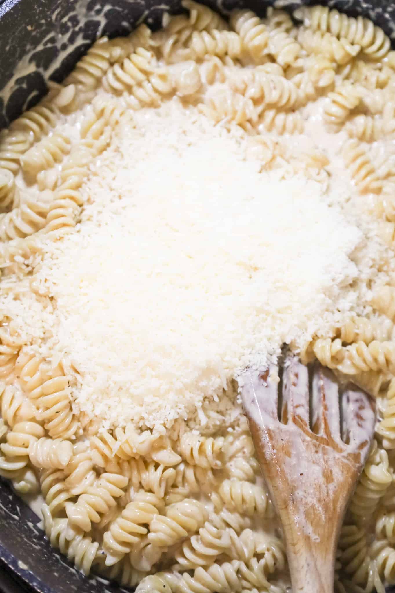 shredded parmesan cheese on top of creamy rotini pasta in a skillet