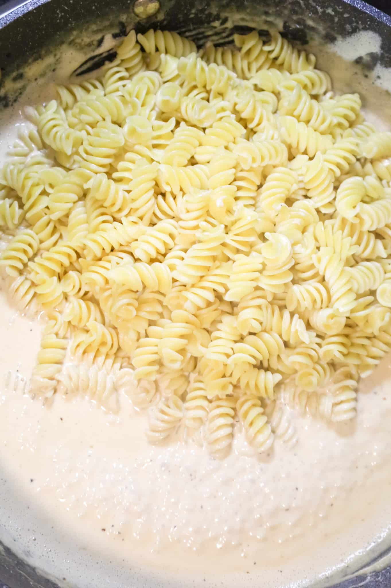 cooked rotini pasta added to a skillet with cream sauce