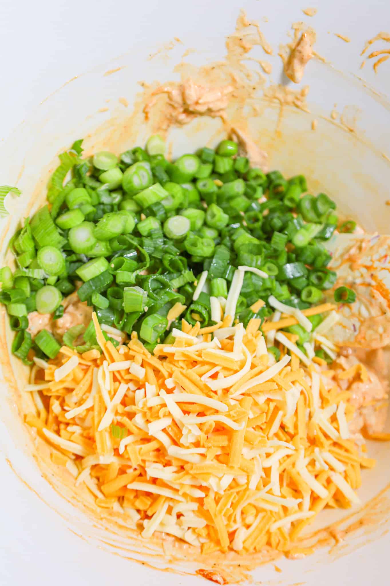 chopped green onions and shredded cheddar cheese on top of buffalo chicken mixture in a mixing bowl