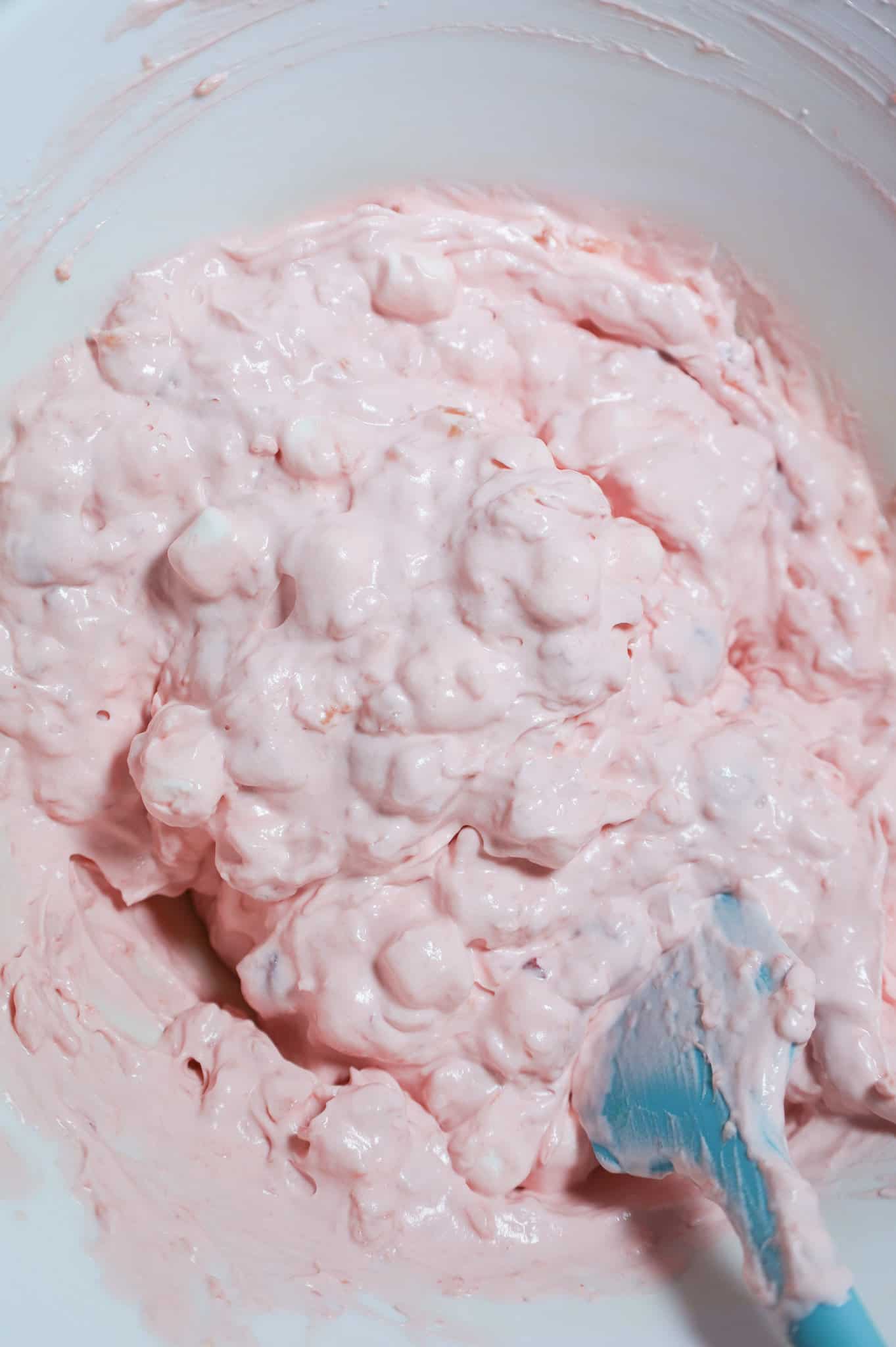 mini marshmallows being stirred into cherry fluff mixture in a mixing bowl