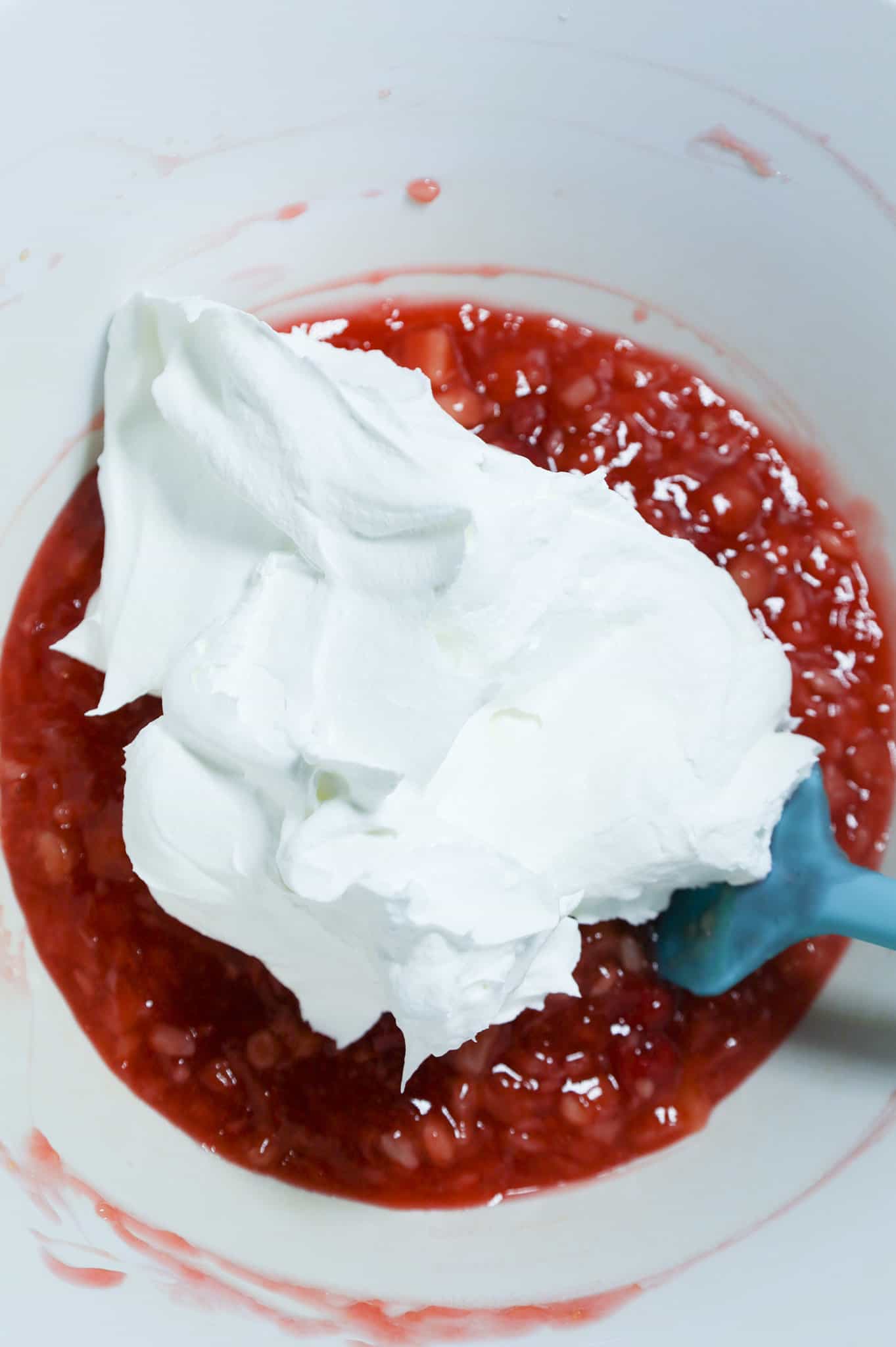 cool whip on top of cherry pie filling, pineapple and pudding mixture in a mixing bowl