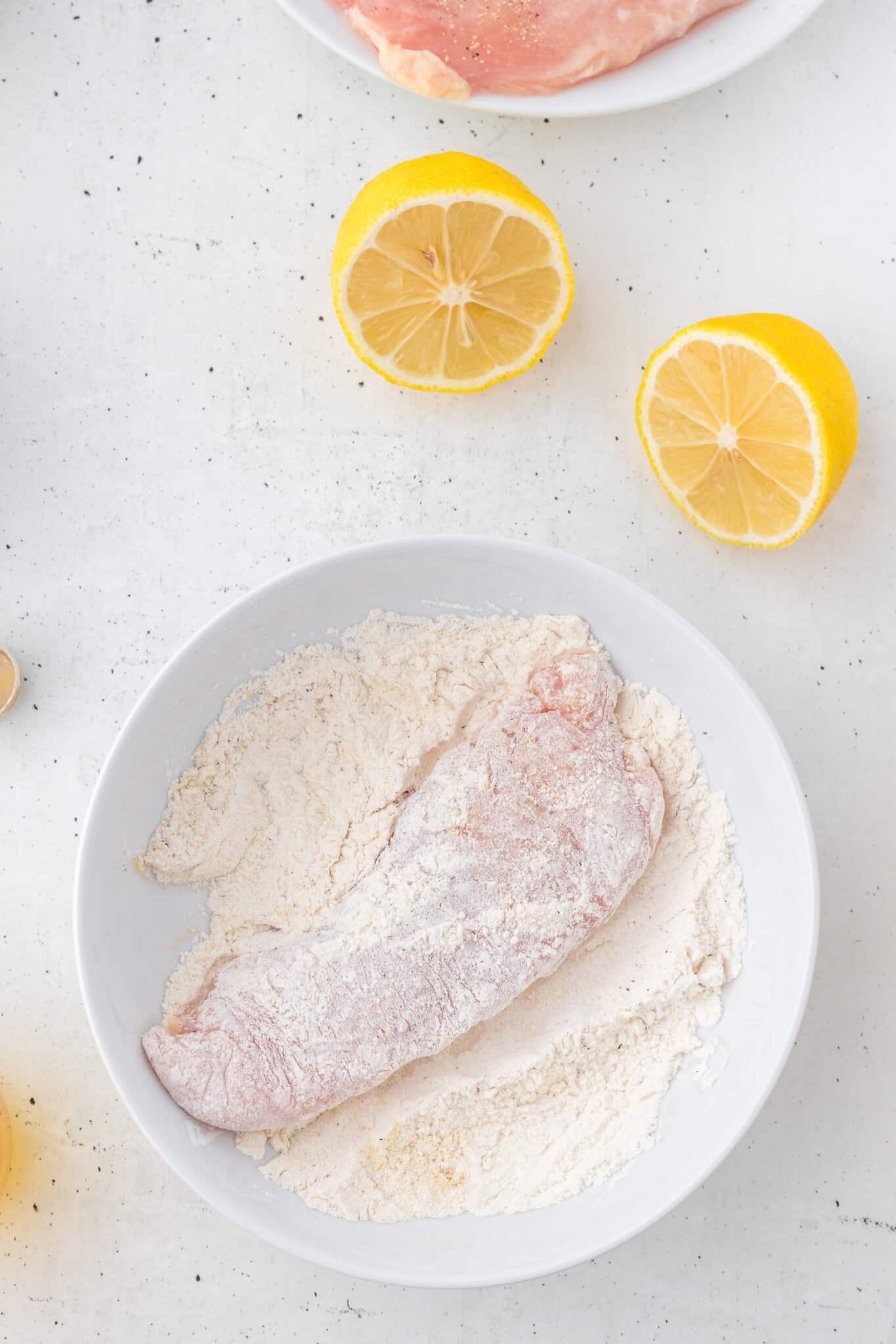 chicken breast being dredged in flour in a bowl
