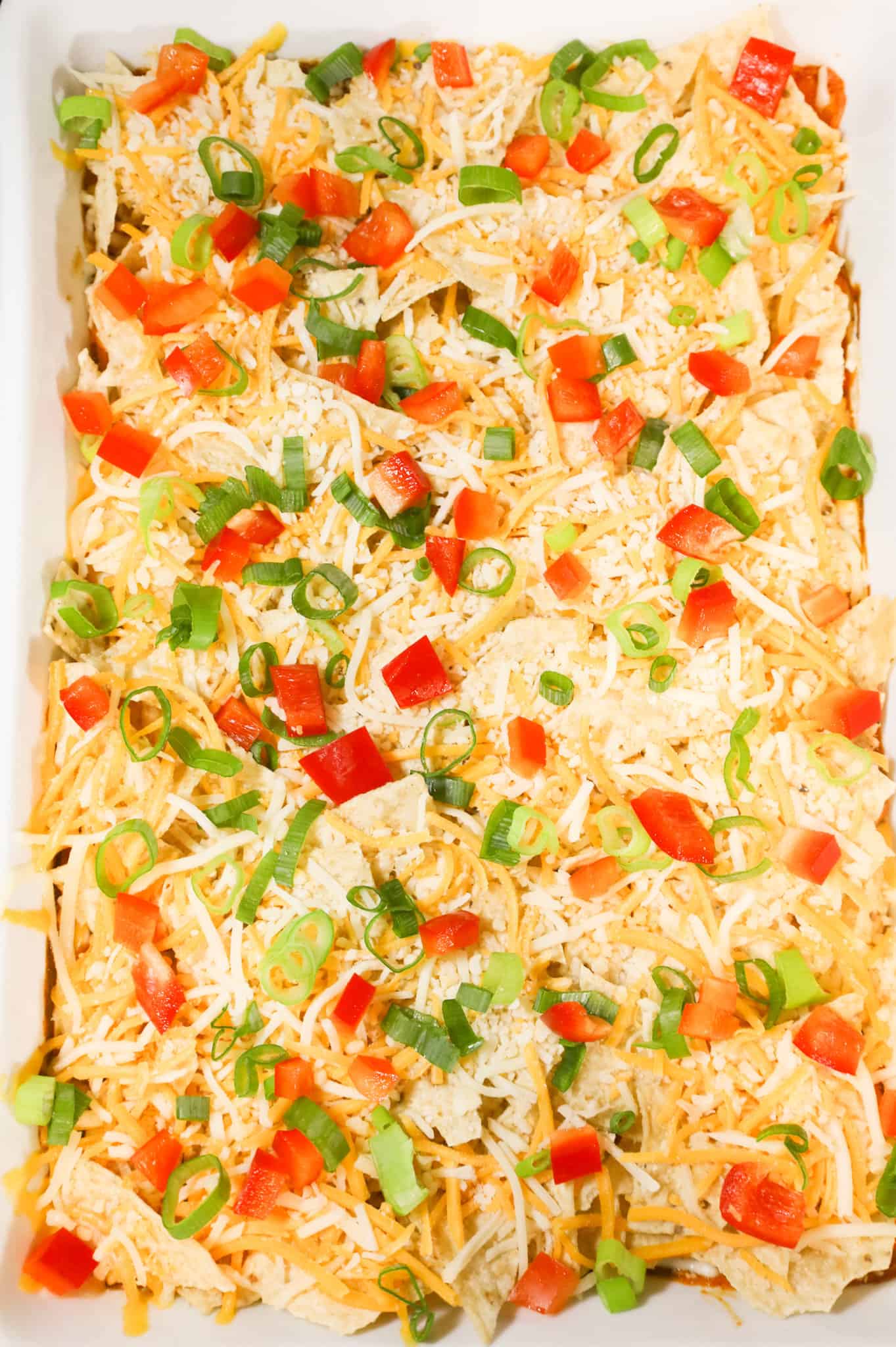 diced red peppers, chopped green onions, shredded cheese and crumbled tortilla chips on top of chicken mixture in a baking dish