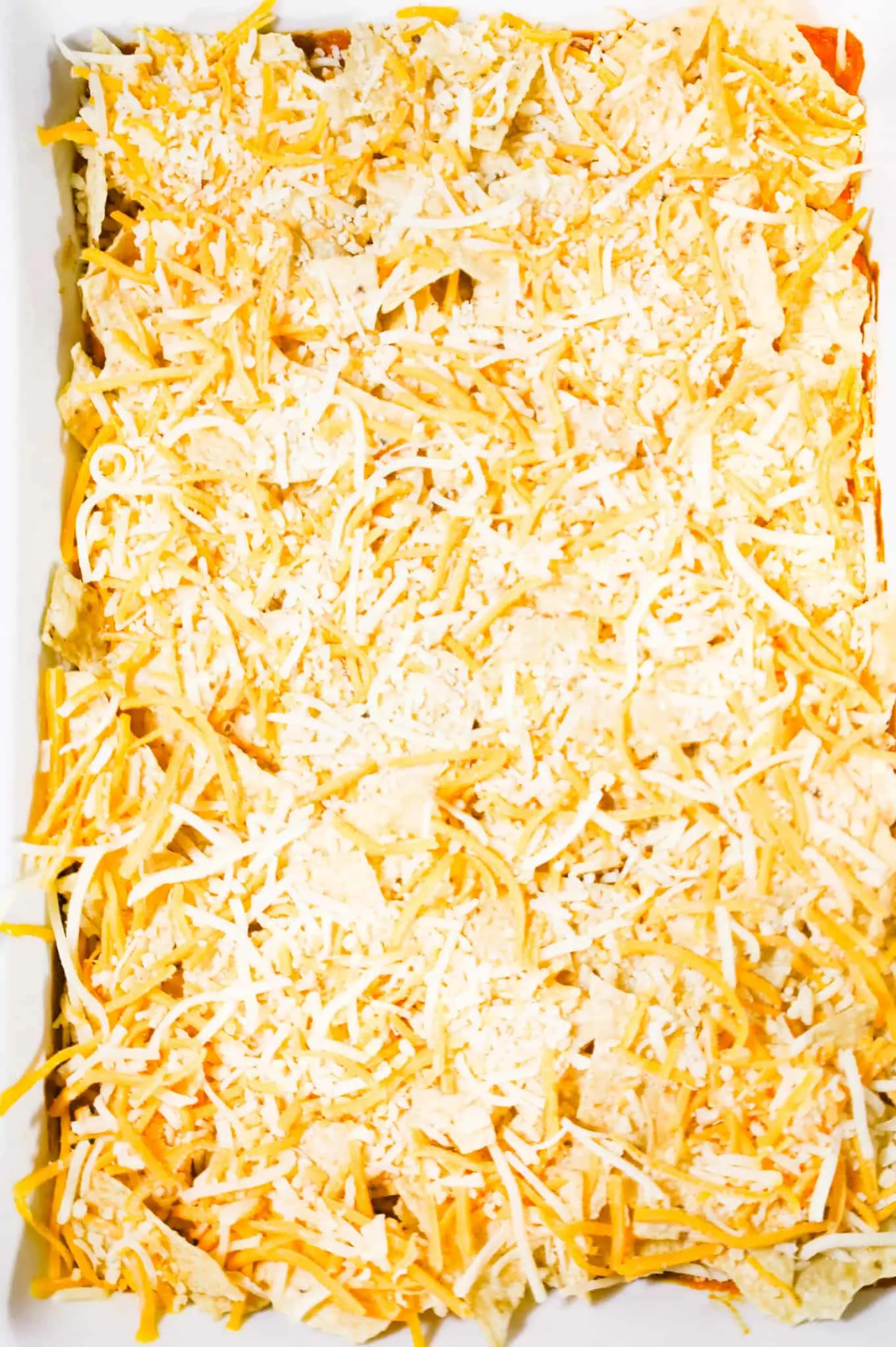 shredded cheese on top of crumbled tortilla chips in a baking dish