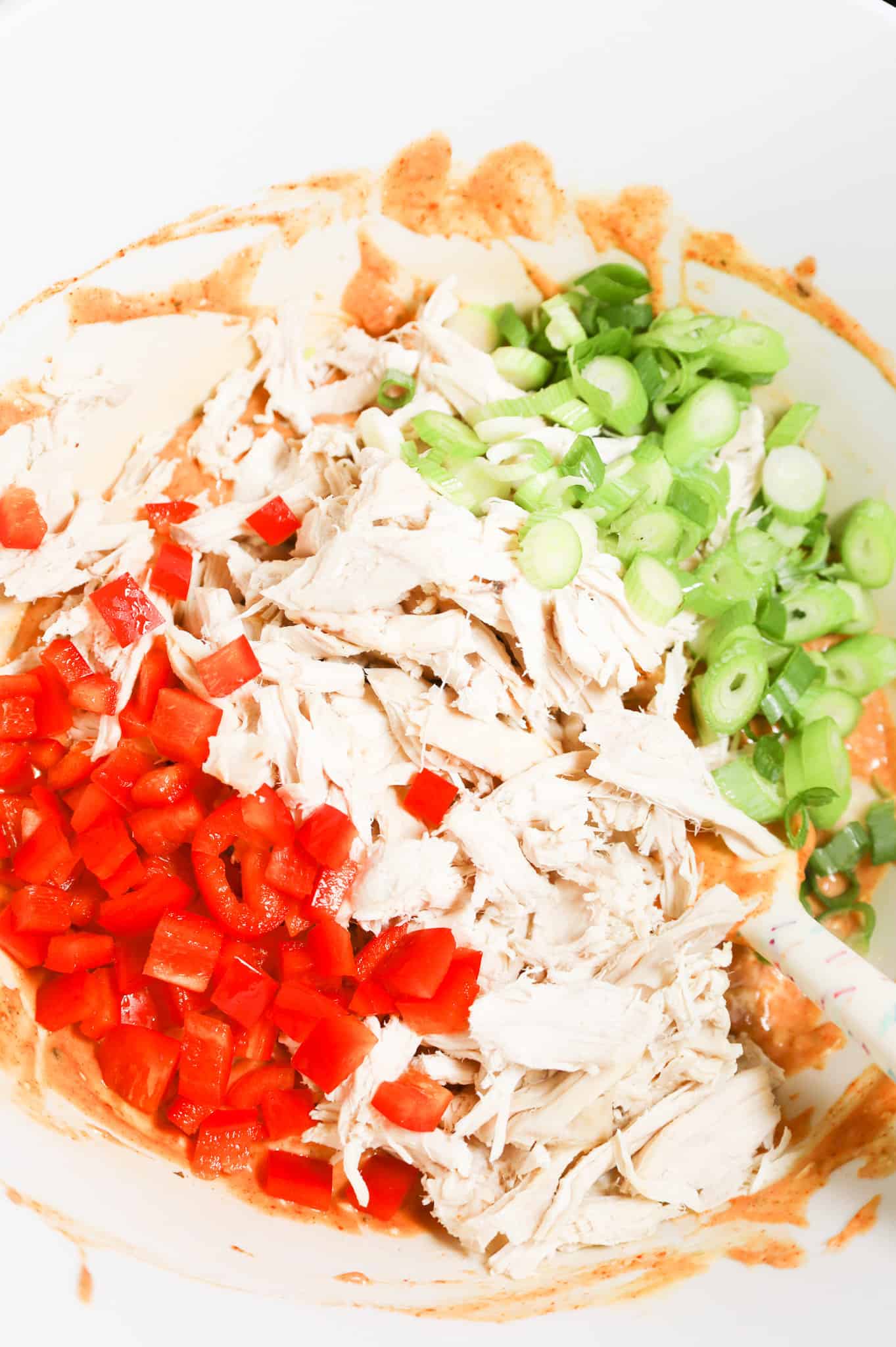 shredded rotisserie chicken, diced red bell peppers and chopped green onions on top of soup and salsa mixture in a mixing bowl