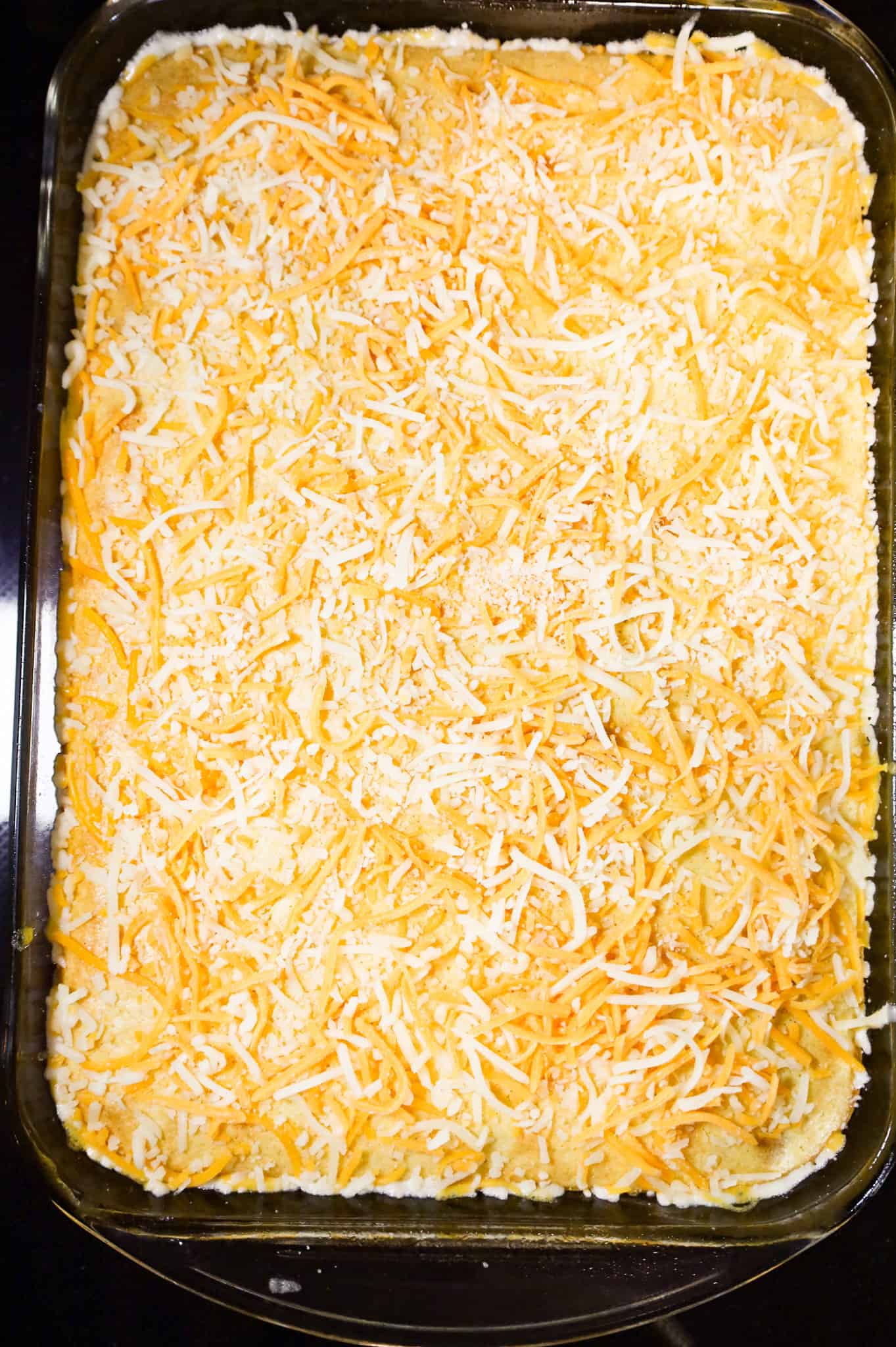 shredded cheese on top of cornbread casserole in a baking dish