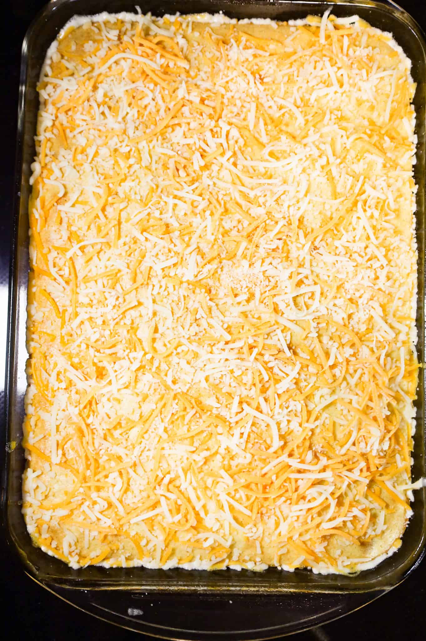 shredded cheese on top of cornbread casserole in a baking dish