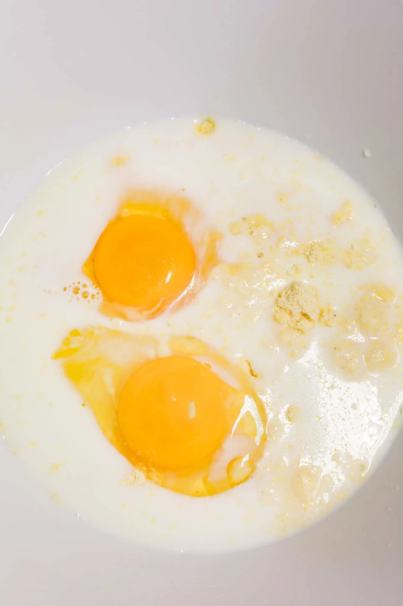 eggs and milk on top of cornbread mix in a mixing bowl