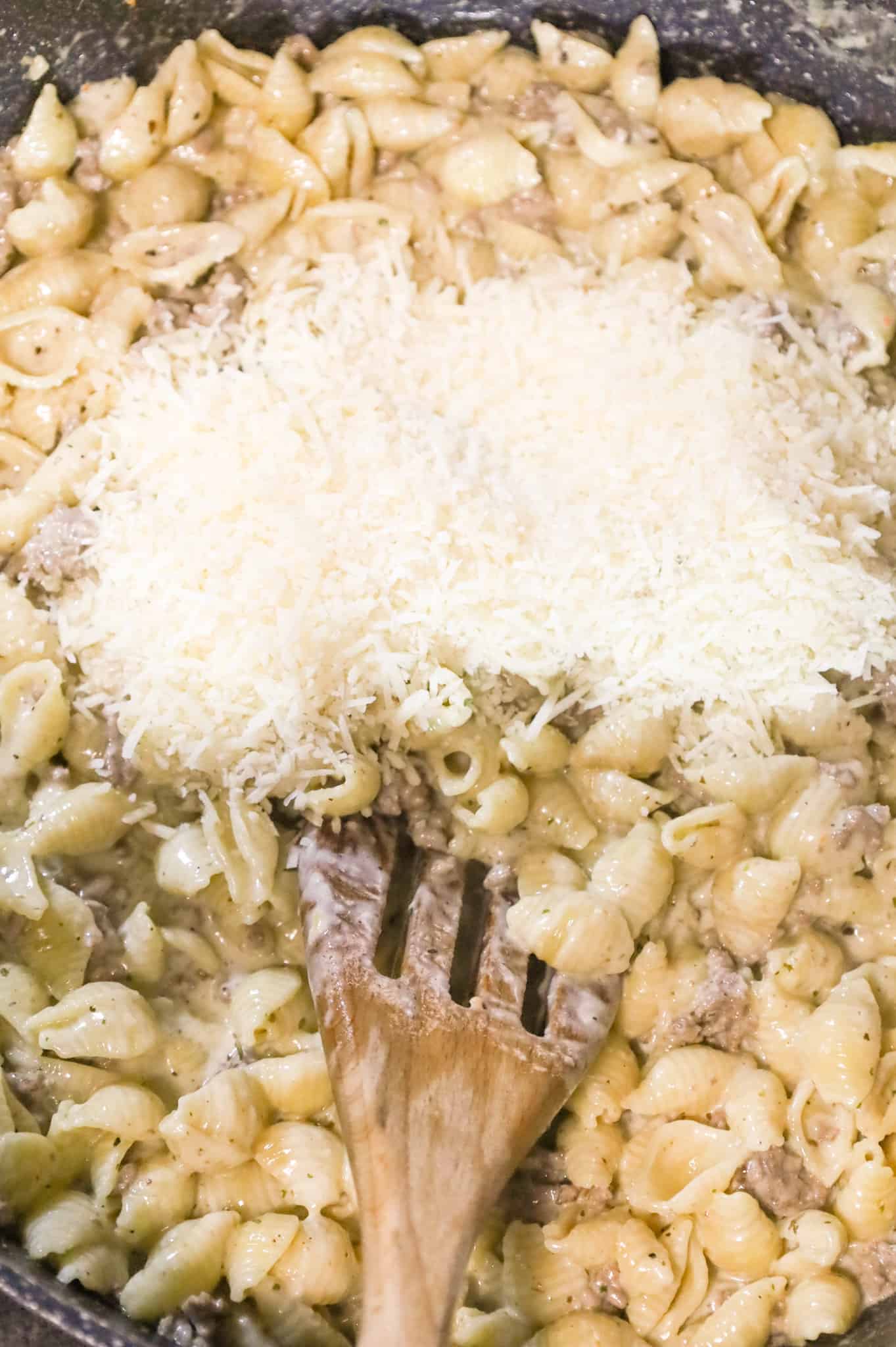 shredded parmesan cheese on top of creamy pasta shells in a skillet