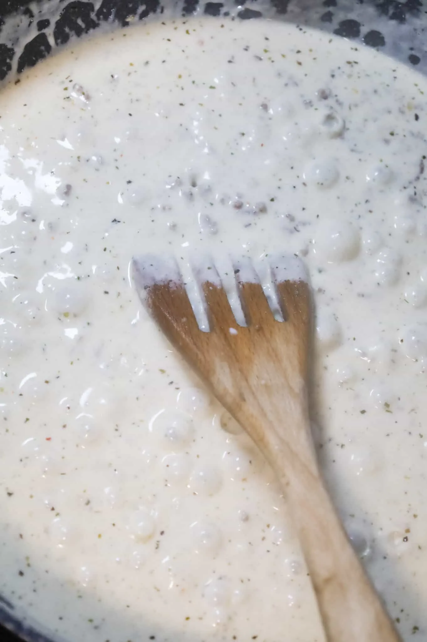 stirring bubbling alfredo sauce in a skillet