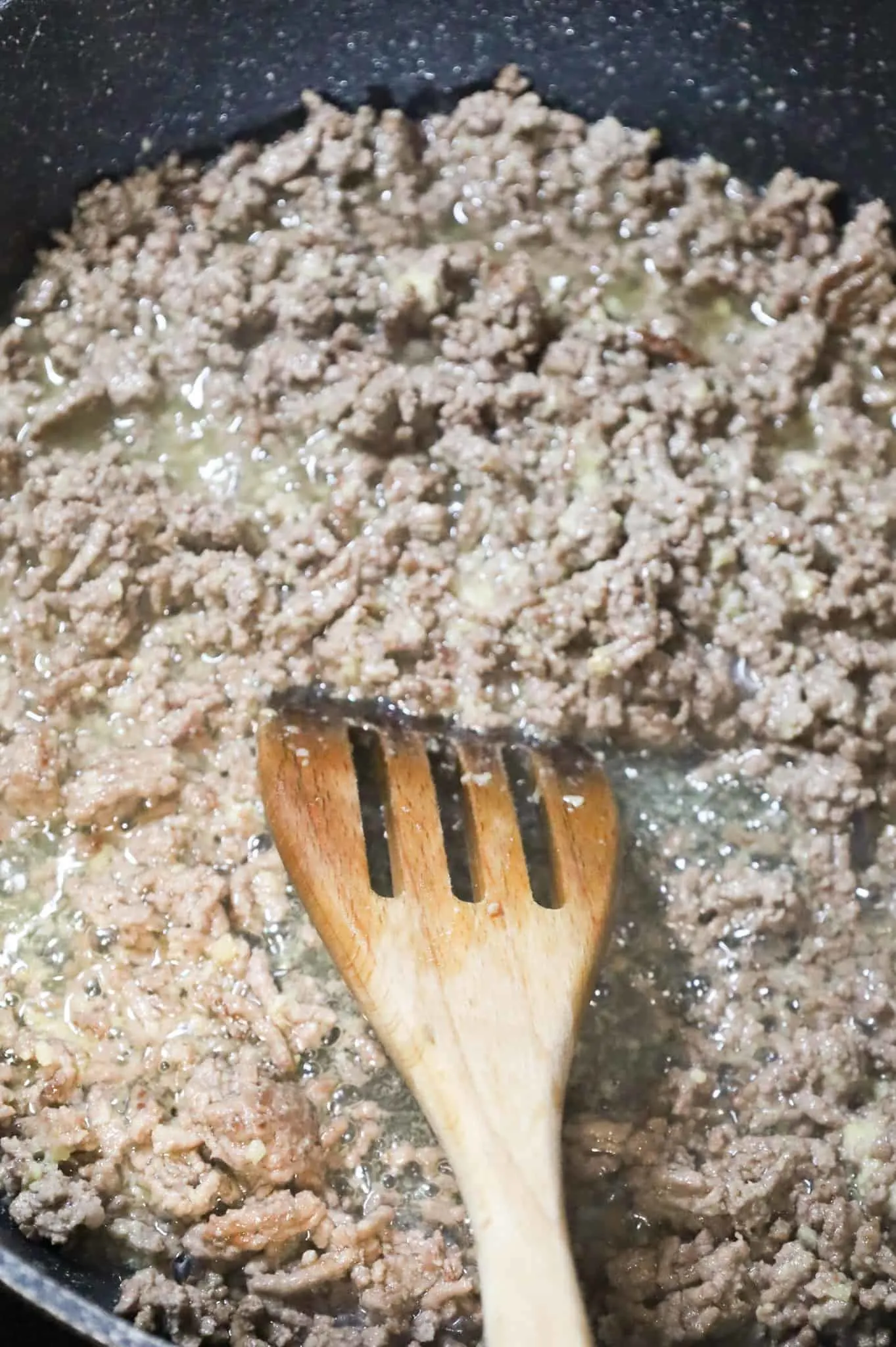 ground beef, butter, and garlic puree being stirred in a skillet