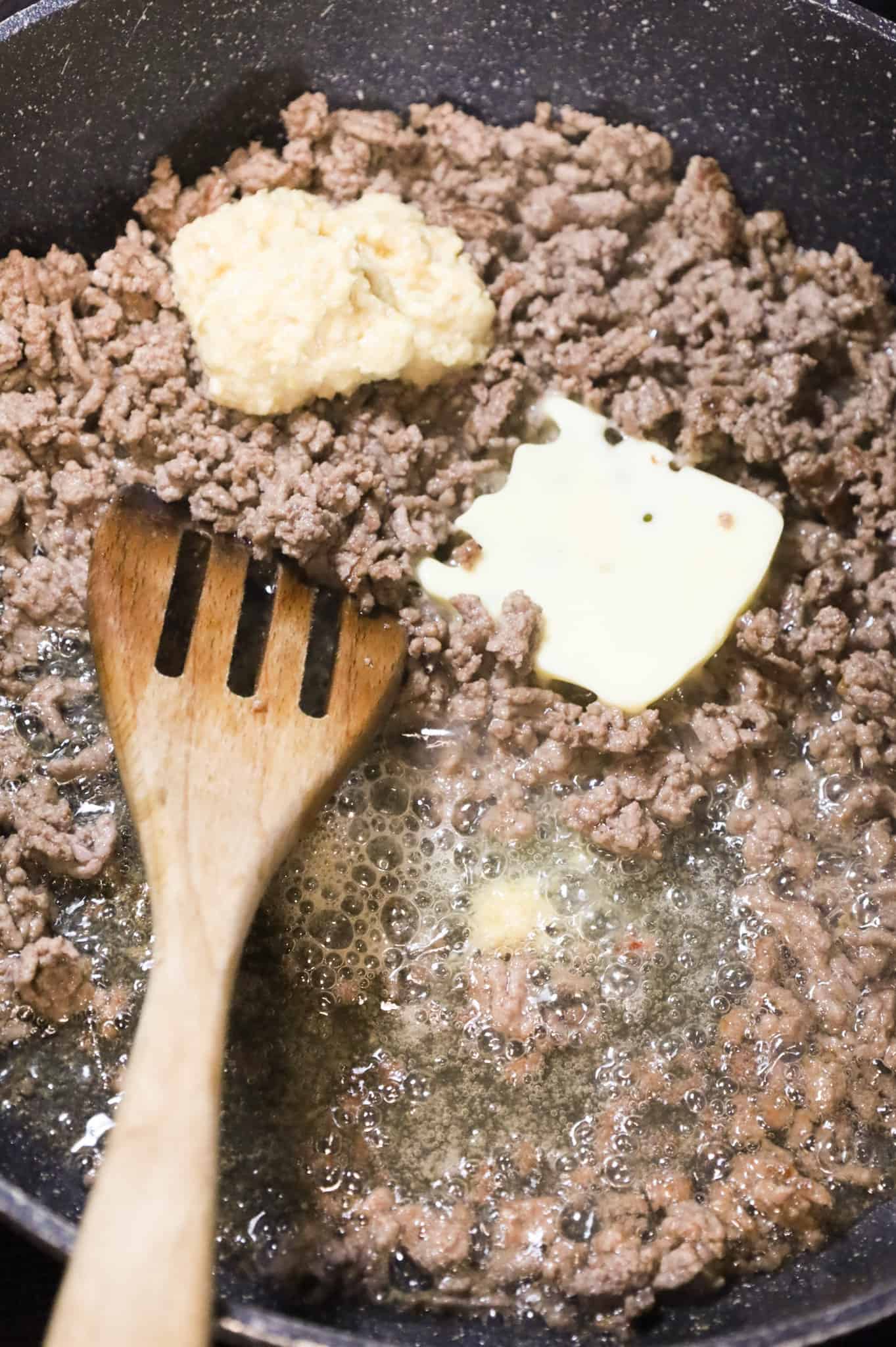 butter and garlic puree on top of cooked ground beef in a skillet