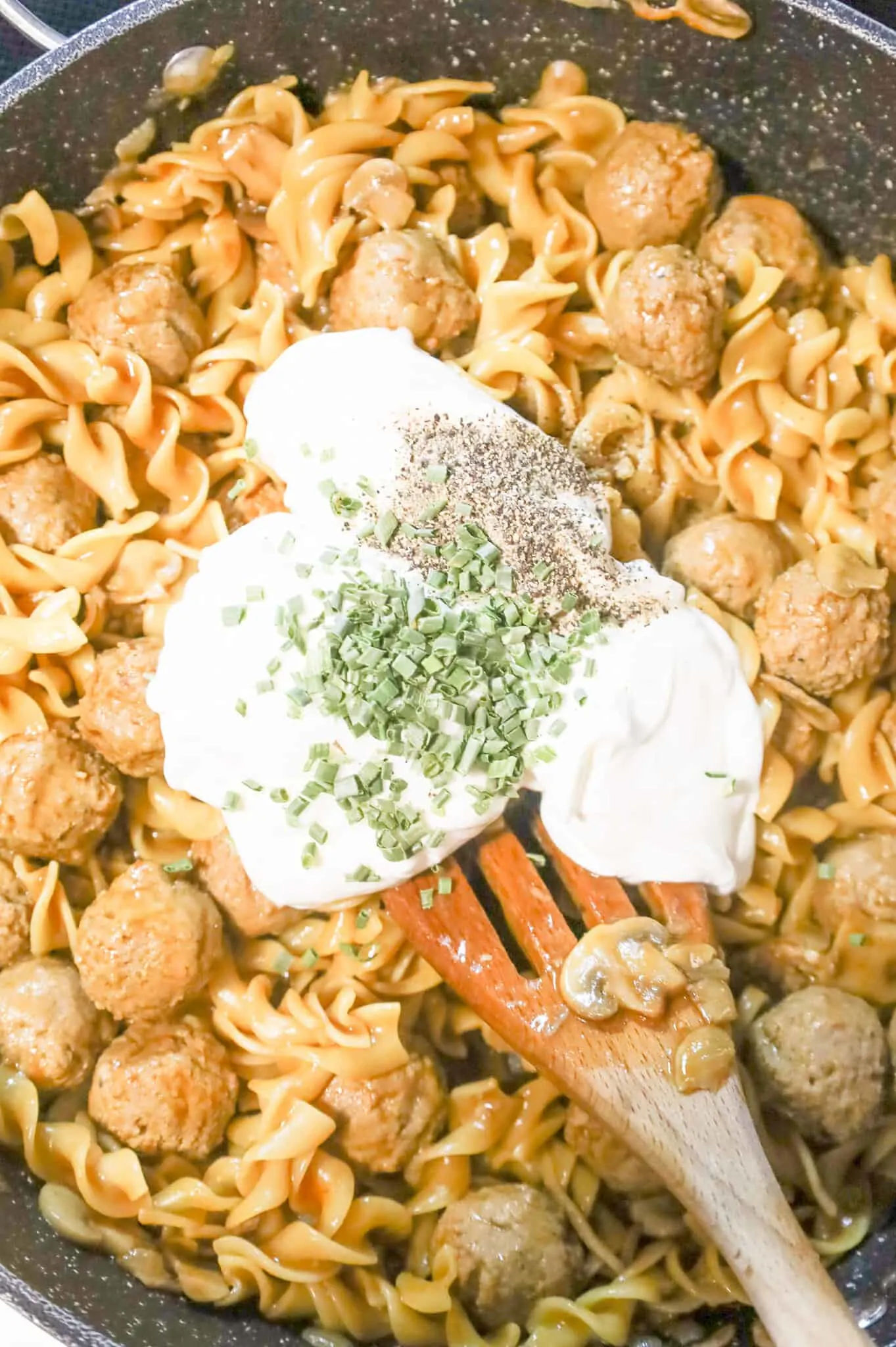 sour cream, salt, pepper and chopped chives on top of meatballs and egg noodles in a skillet
