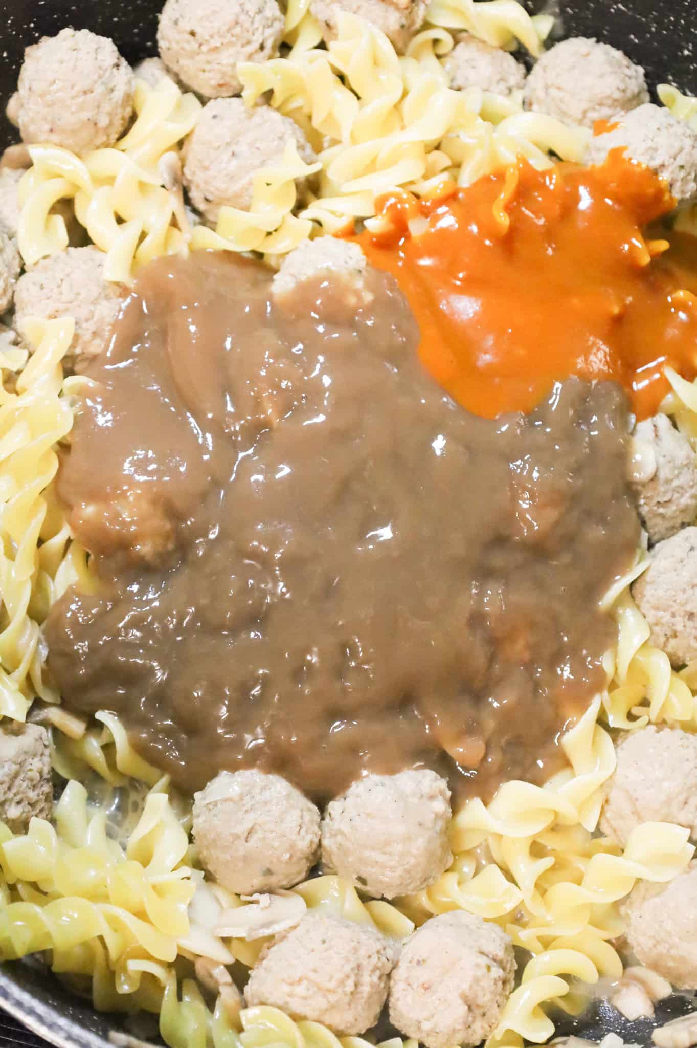 beef gravy and Heinz 57 sauce on top of meatballs and egg noodles in a skillet