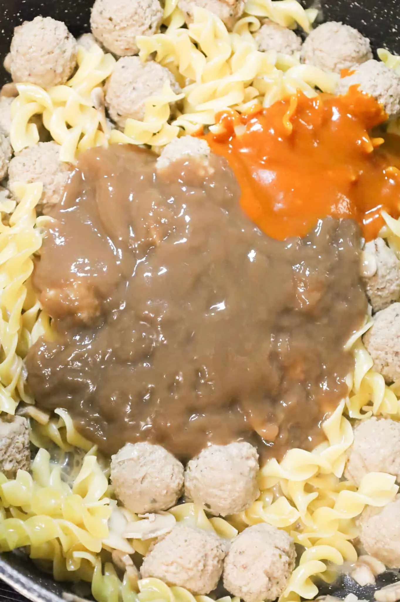 beef gravy and Heinz 57 sauce on top of meatballs and egg noodles in a skillet