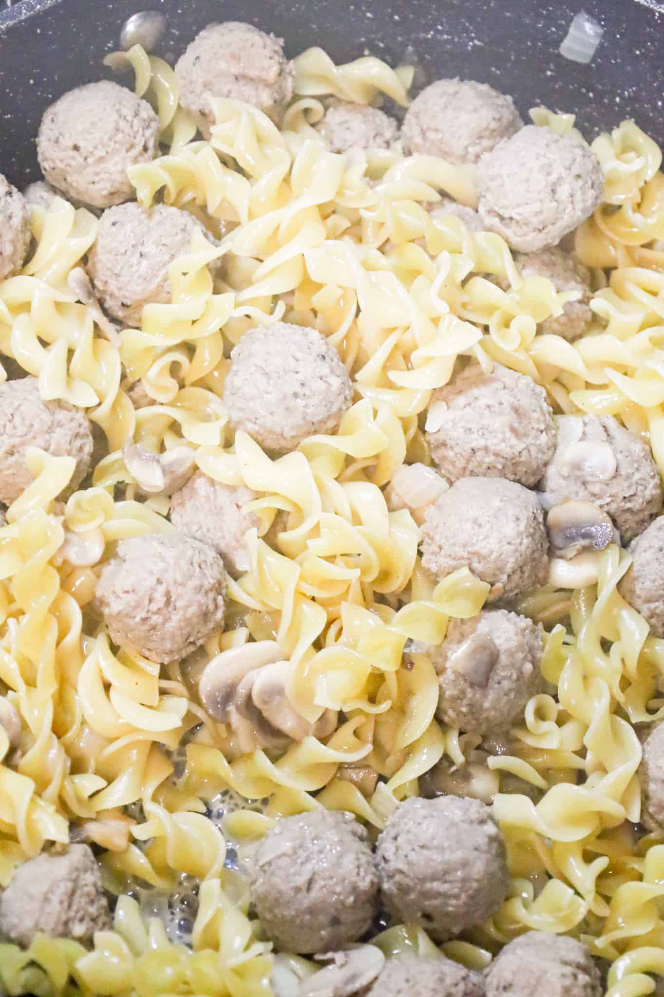 egg noodles cooking with meatballs in a skillet