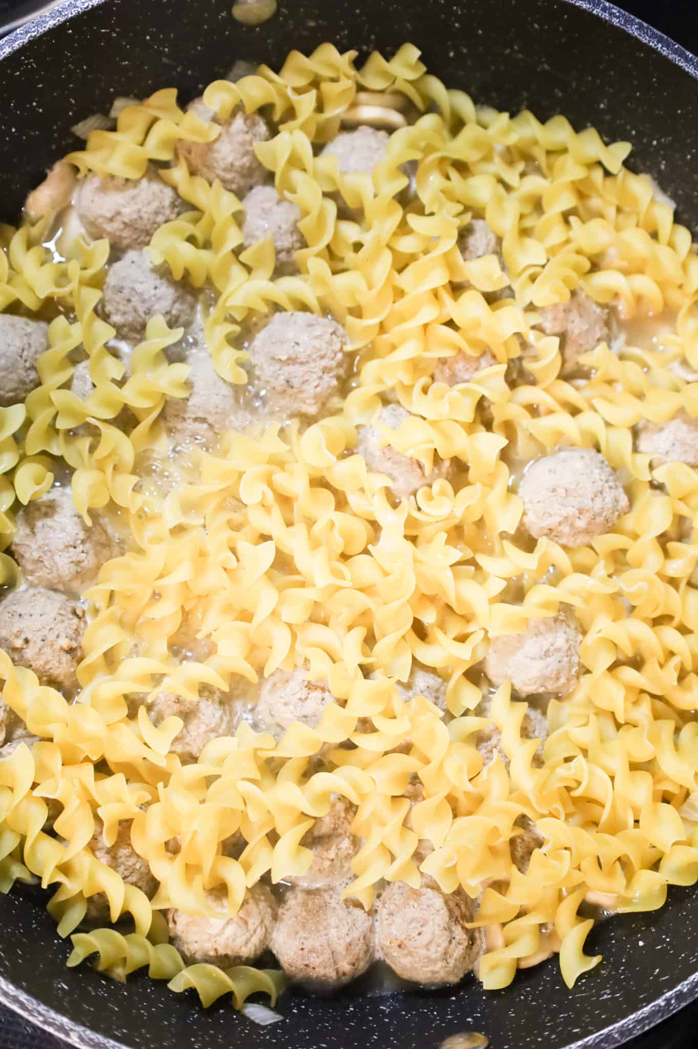 egg noodles being stirred with meatballs in a skillet