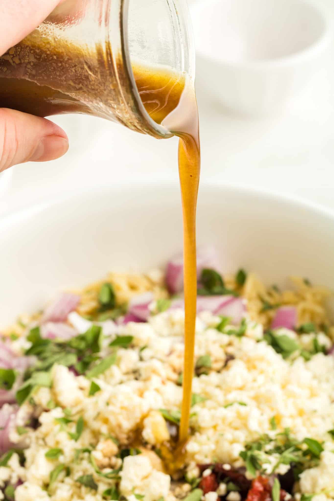 balsamic dressing being poured over feta and oregano orzo pasta salad