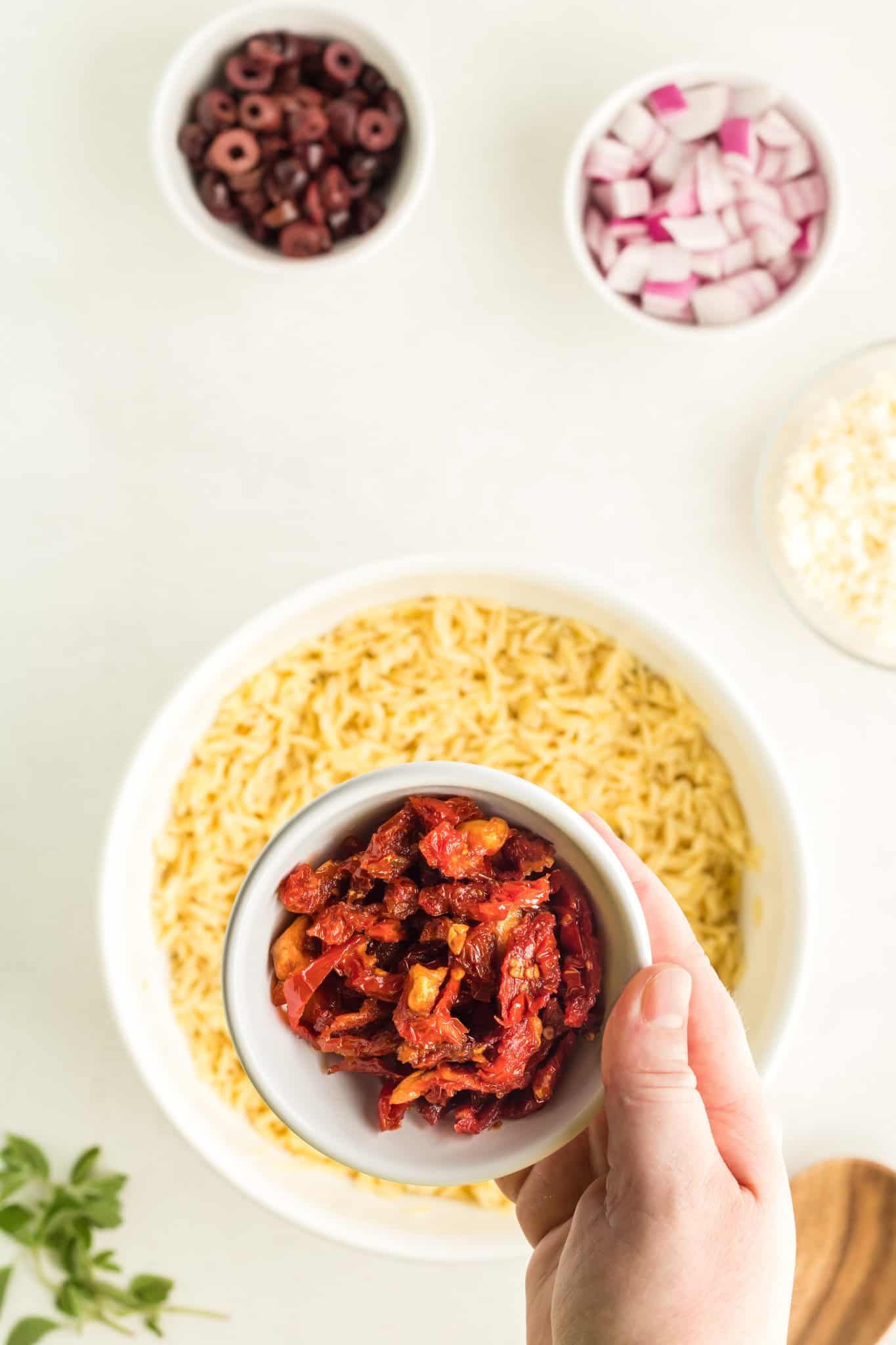 sun dried tomatoes being added to orzo pasta in a bowl