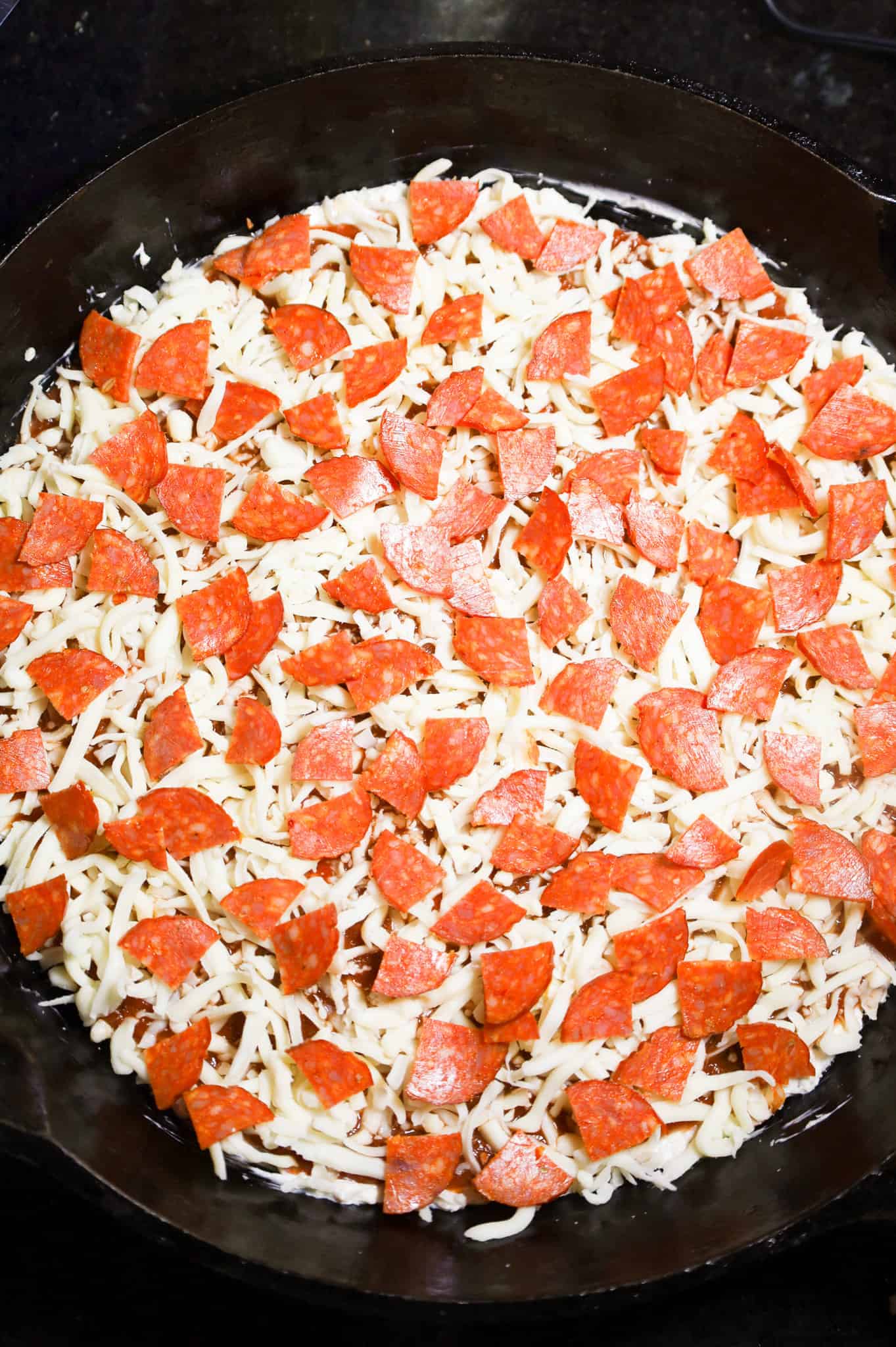 chopped pepperoni on top of pizza dip in a skillet