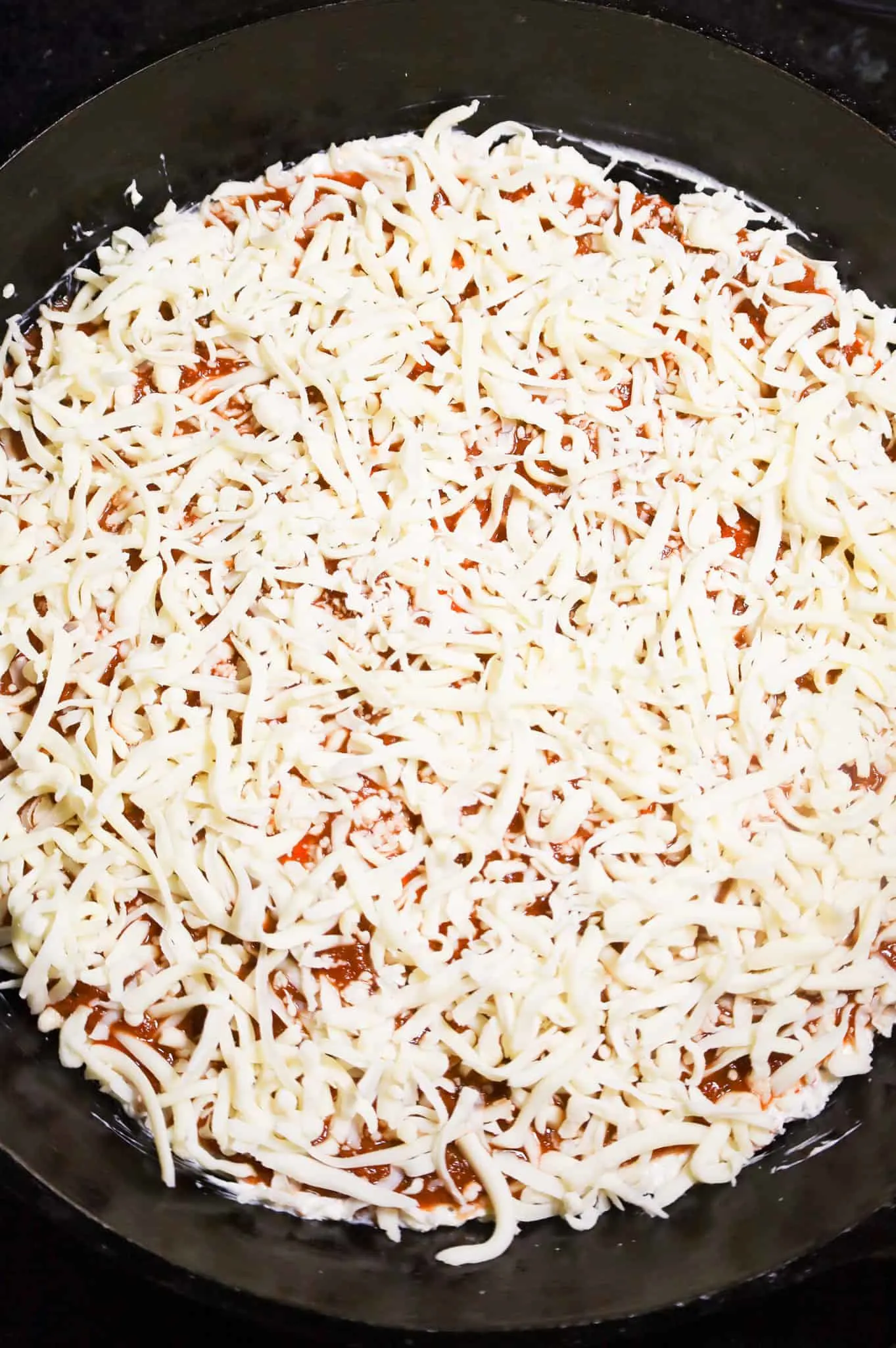 shredded mozzarella cheese on top of pizza sauce and cream cheese mixture in a skillet