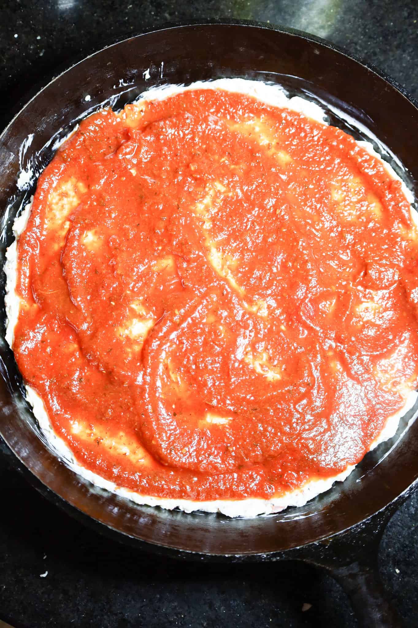 pizza sauce spread on top of cream cheese mixture in a cast iron skillet