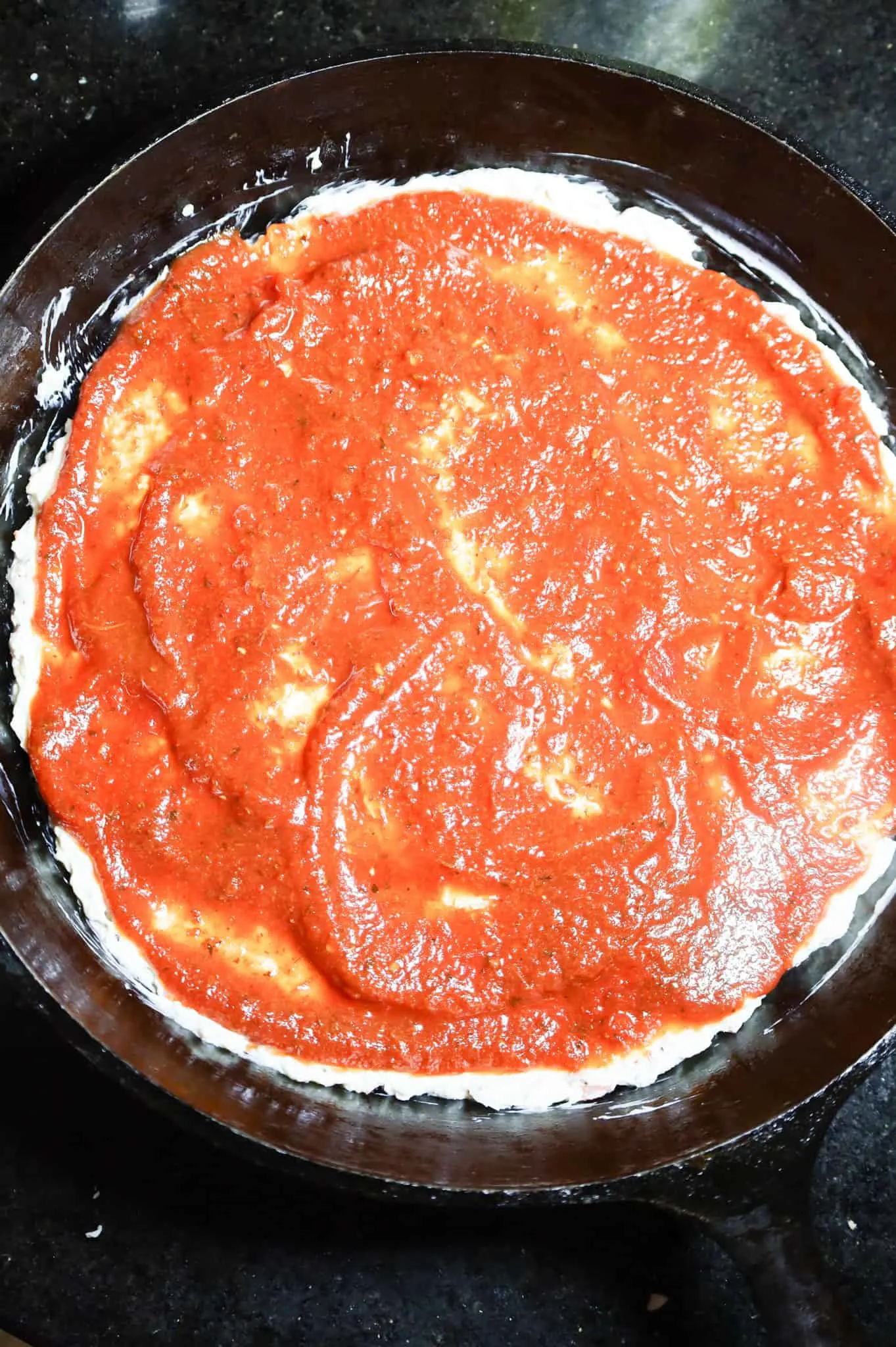 pizza sauce spread on top of cream cheese mixture in a cast iron skillet