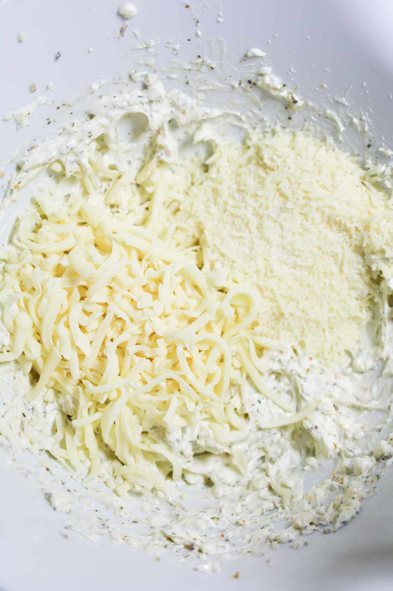 shredded mozzarella cheese and grated parmesan cheese on top of cream cheese mixture in a mixing bowl