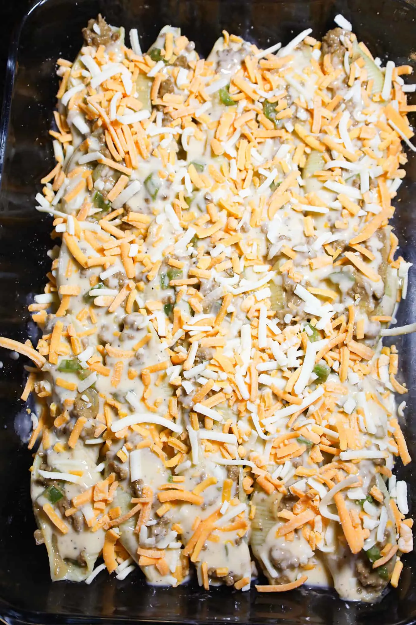 shredded cheddar cheese on top of stuffed pasta shells in a baking dish